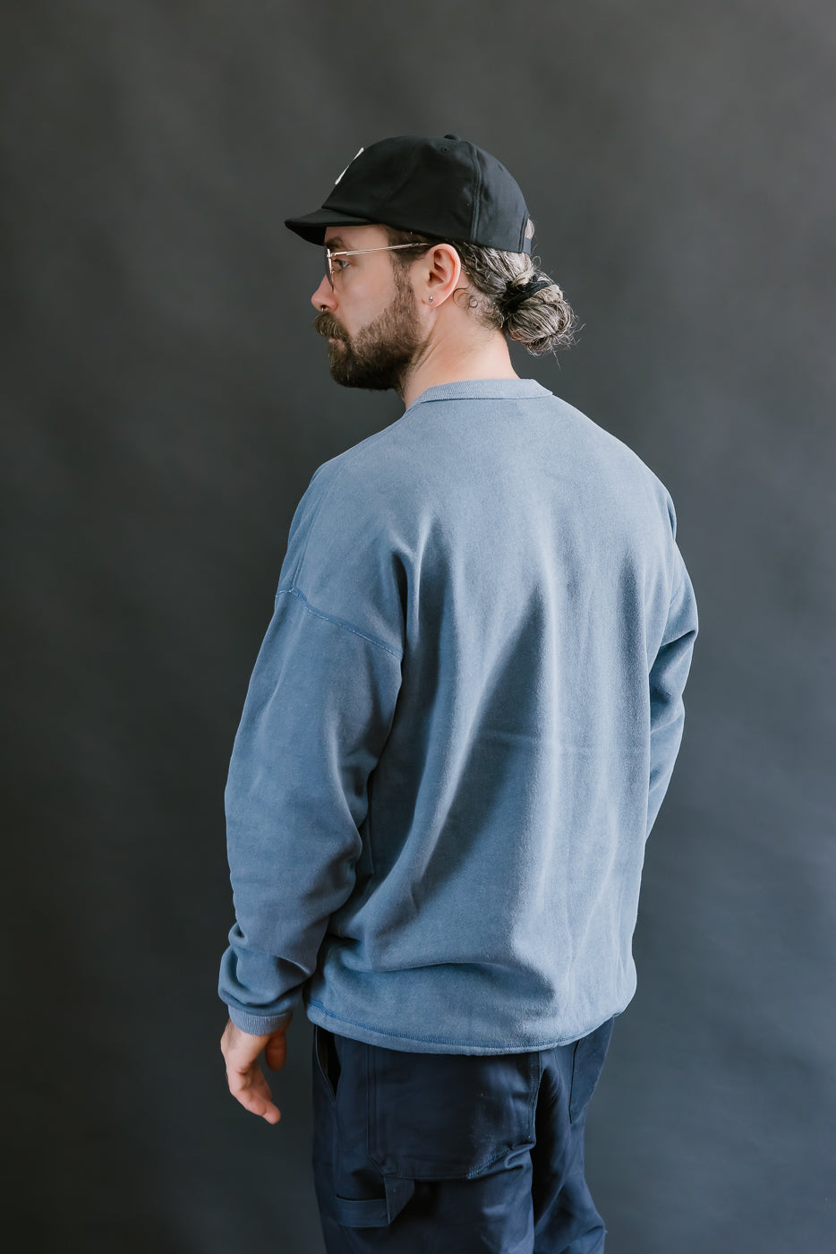 Man wearing a blue sweatshirt and black cap against a dark background