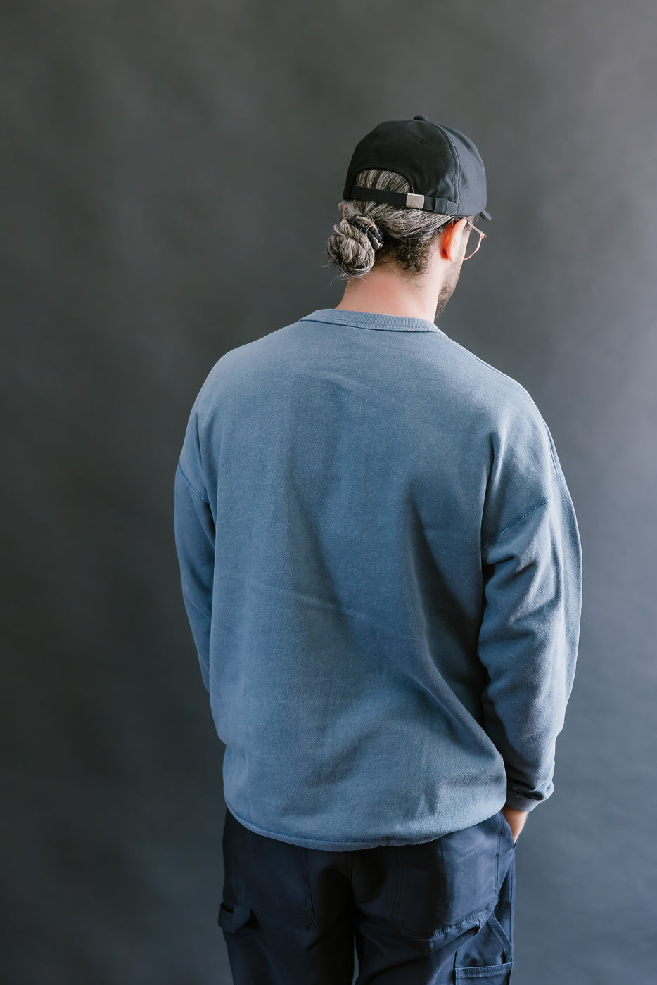Person wearing a blue long-sleeve shirt and black cap against a gray background