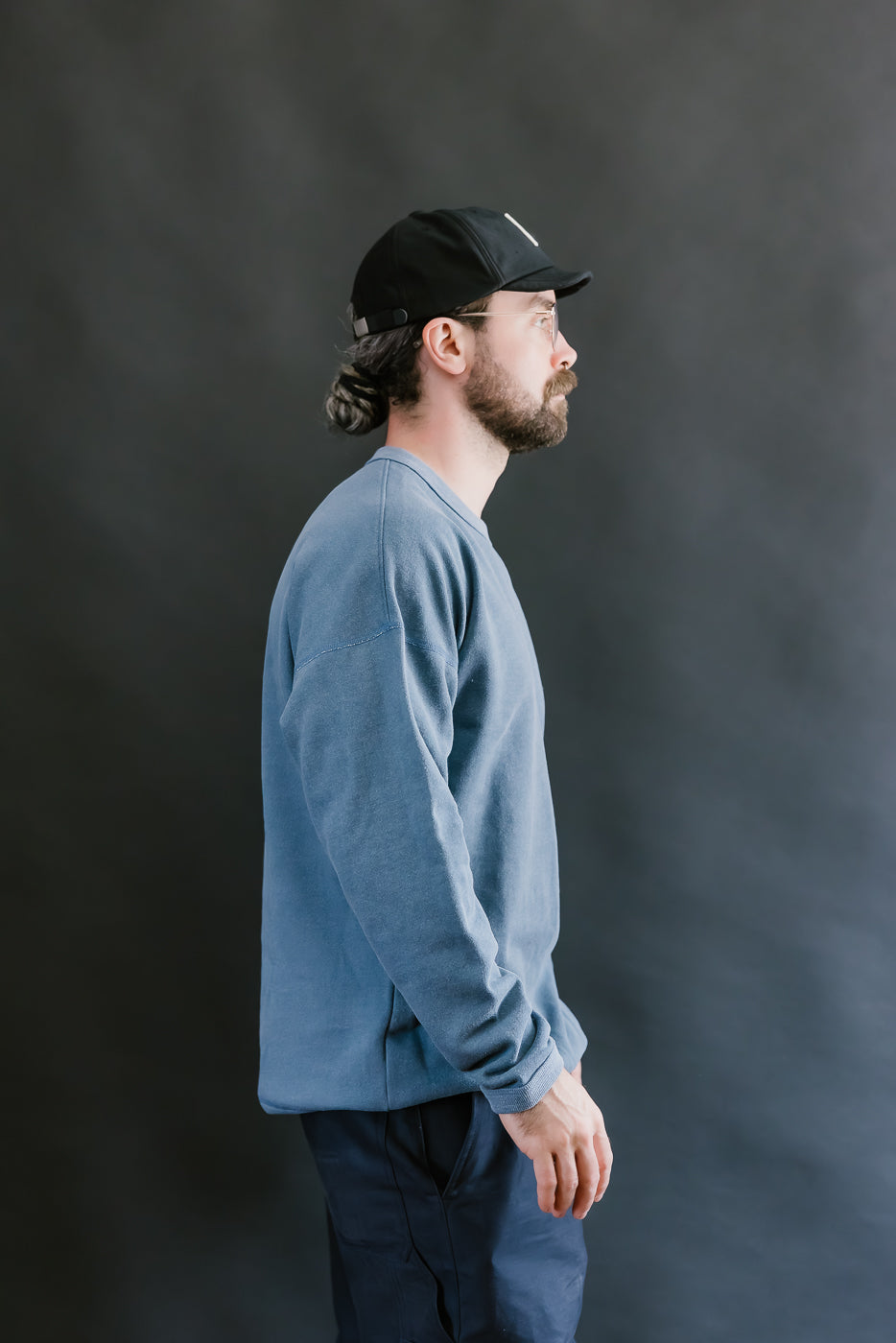 Man wearing a blue sweatshirt and black cap against a dark background