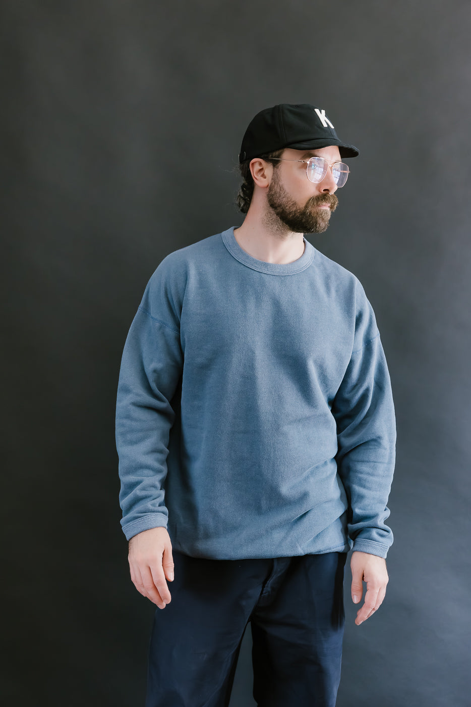 Man wearing a blue sweatshirt and black cap against a dark background