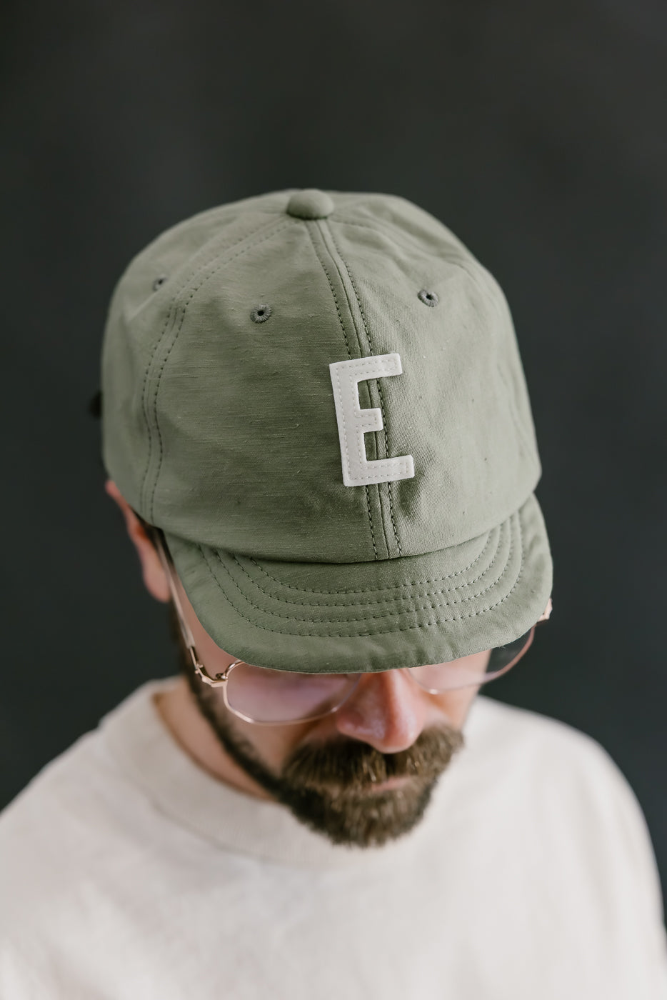 Person wearing a green cap with a white letter 'E' on a dark background