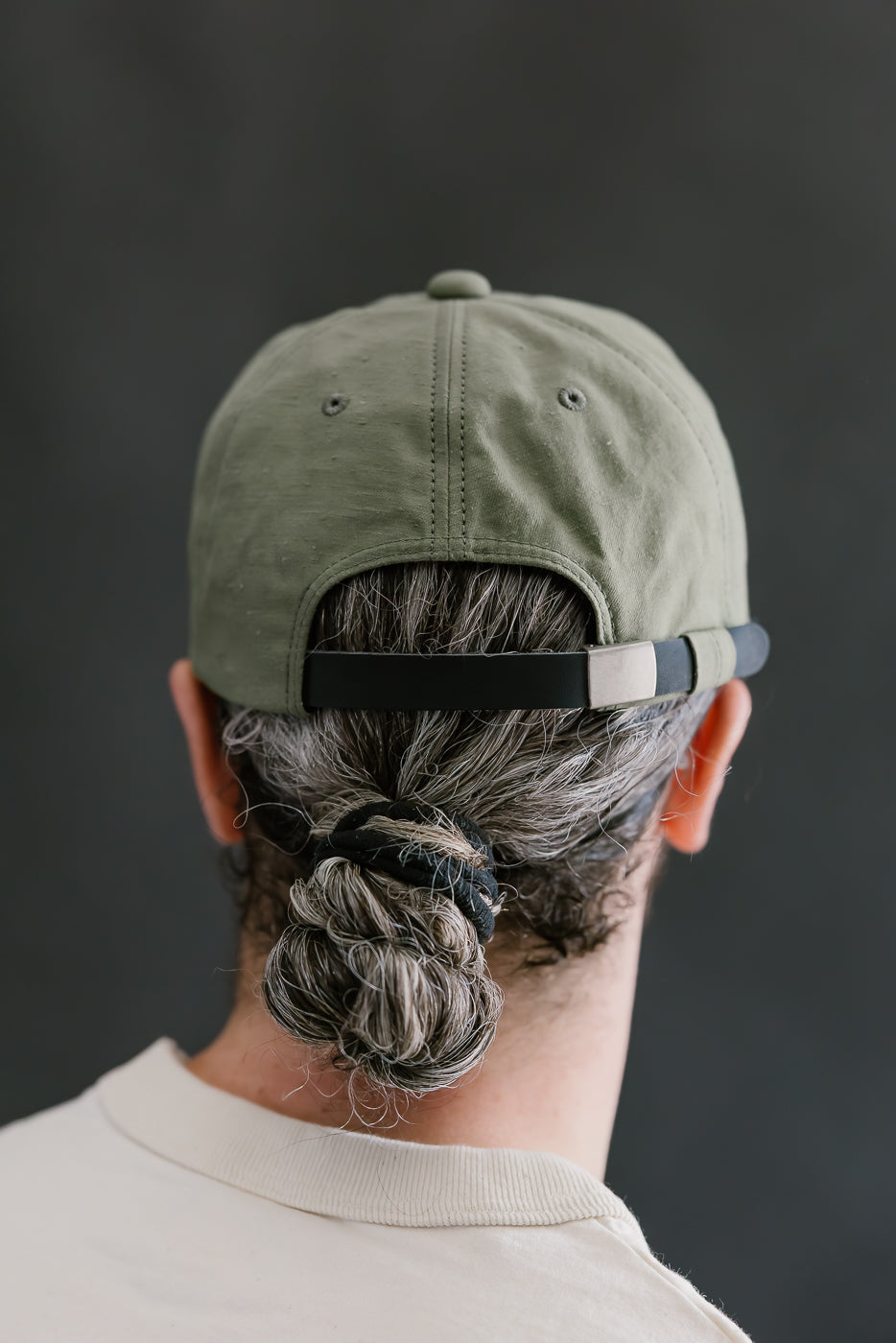 Person wearing a green cap with a black strap, facing away from the camera on a dark background