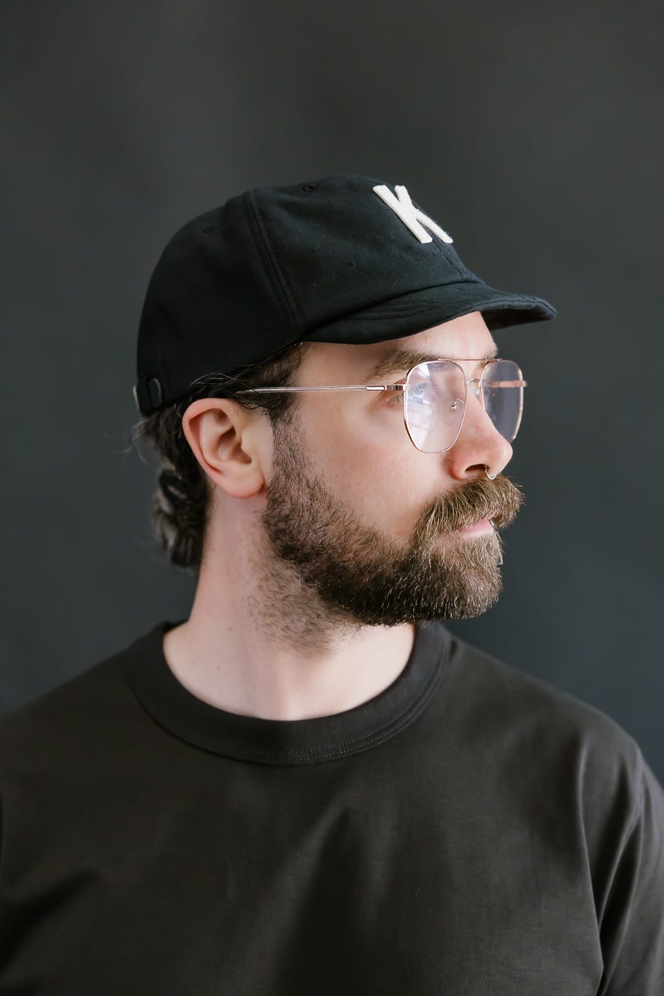 Man wearing a black cap and glasses against a dark background
