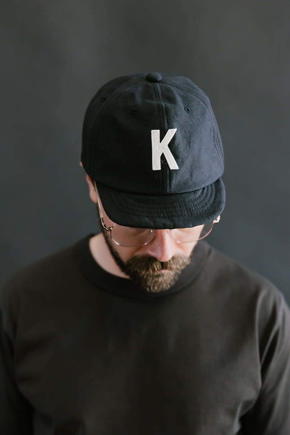 Man wearing a black cap with a white 'K' logo against a dark background