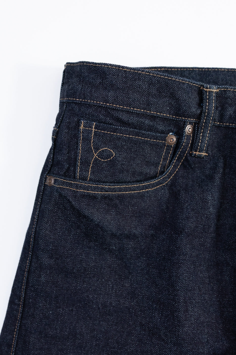 Close-up of dark blue denim jeans with a lasso stitch on the coin pocket against a white background