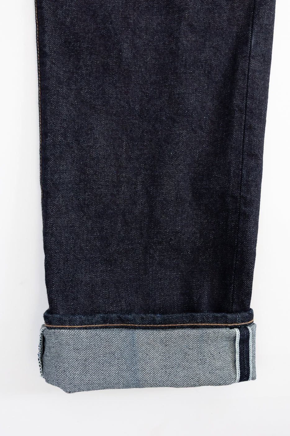 Close-up of the cuff of a dark blue denim jeans with a white background