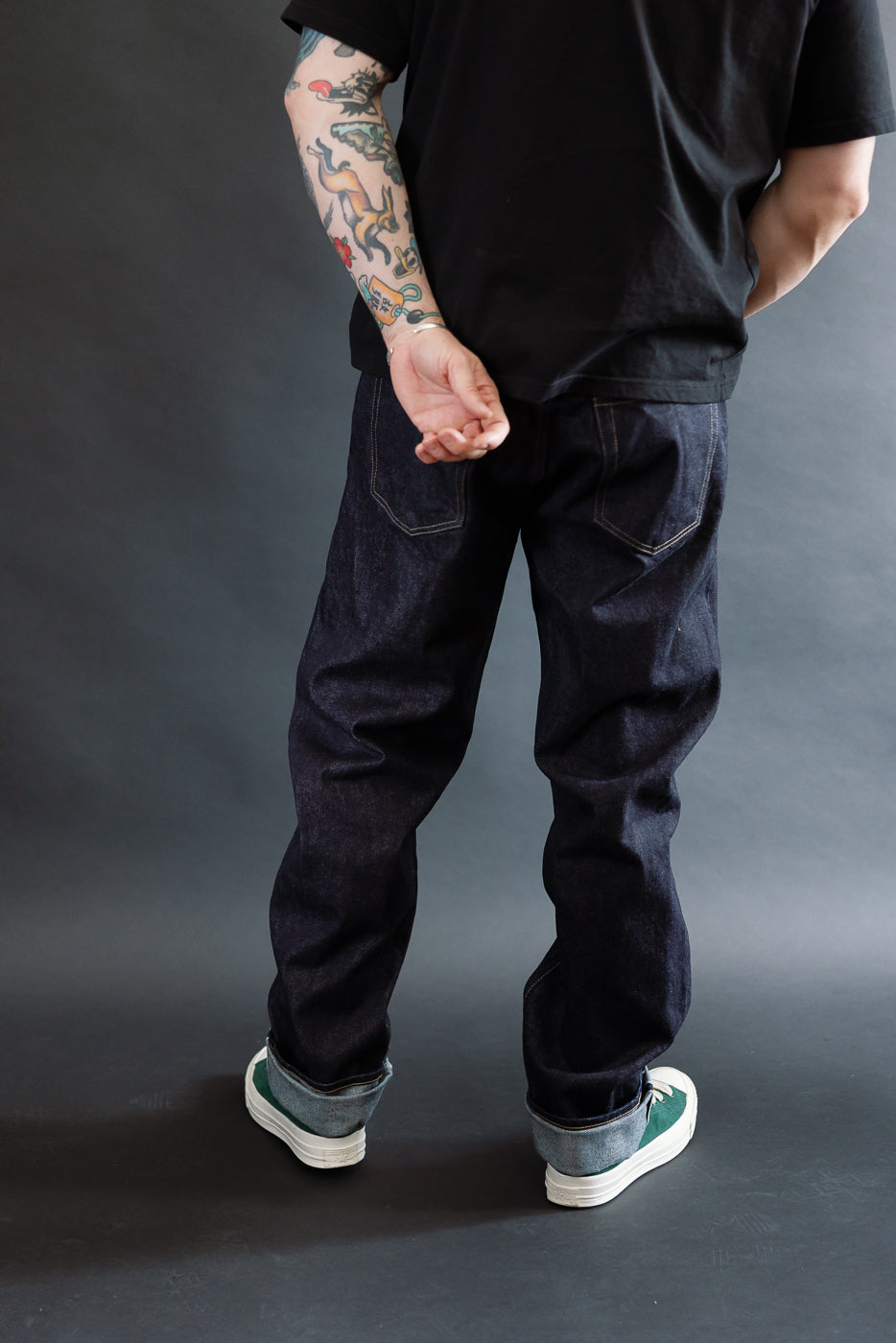 3/4 view, Man wearing a black t-shirt, dark RGT 15oz rinsed selvedge jeans, green shoes, back view