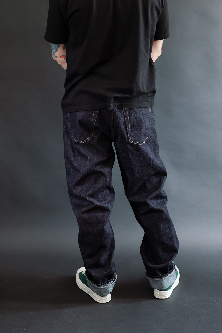 3/4 view, Man wearing a black t-shirt, dark RGT 15oz rinsed selvedge jeans, green shoes, back view
