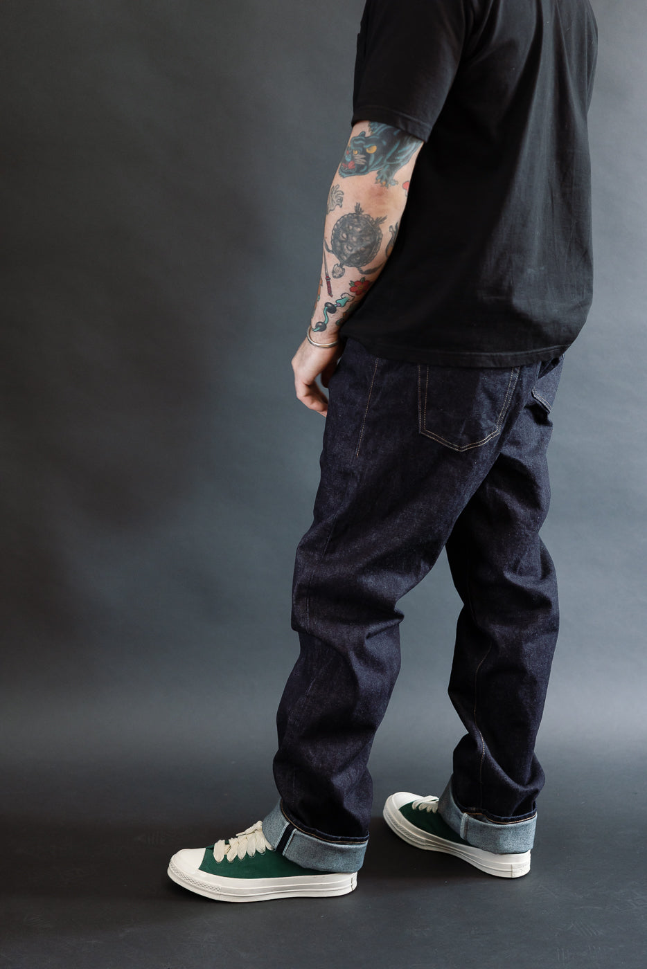 3/4 view, Man wearing a black t-shirt, dark RGT 15oz rinsed selvedge jeans, green shoes, side view