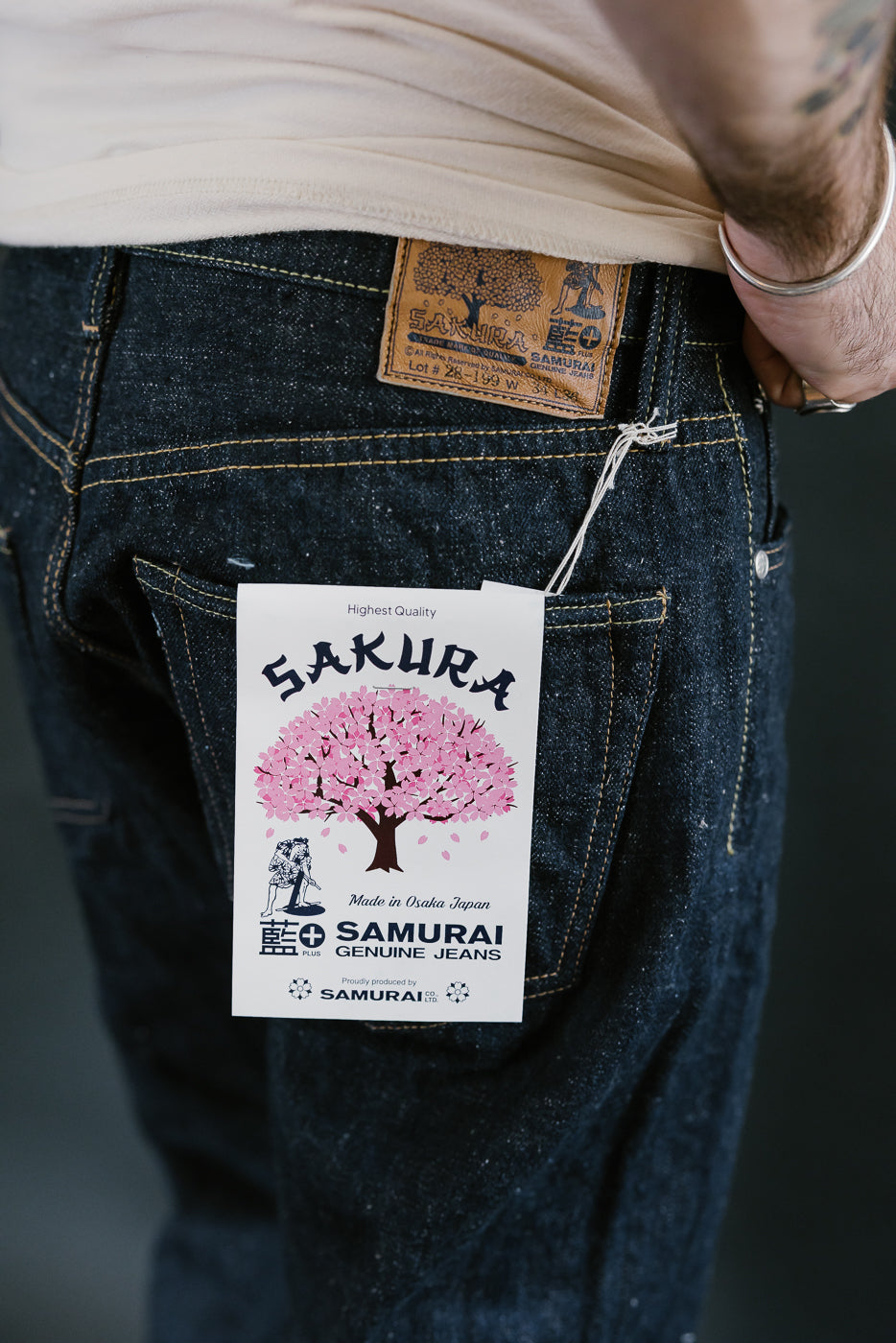 Close-up of Samurai's S500AX-SAKURA jeans, featuring a leather patch and cherry blossom hang-tag, showcasing the 18oz Ai-Plus-Sakura selvedge denim's intricate texture and design.