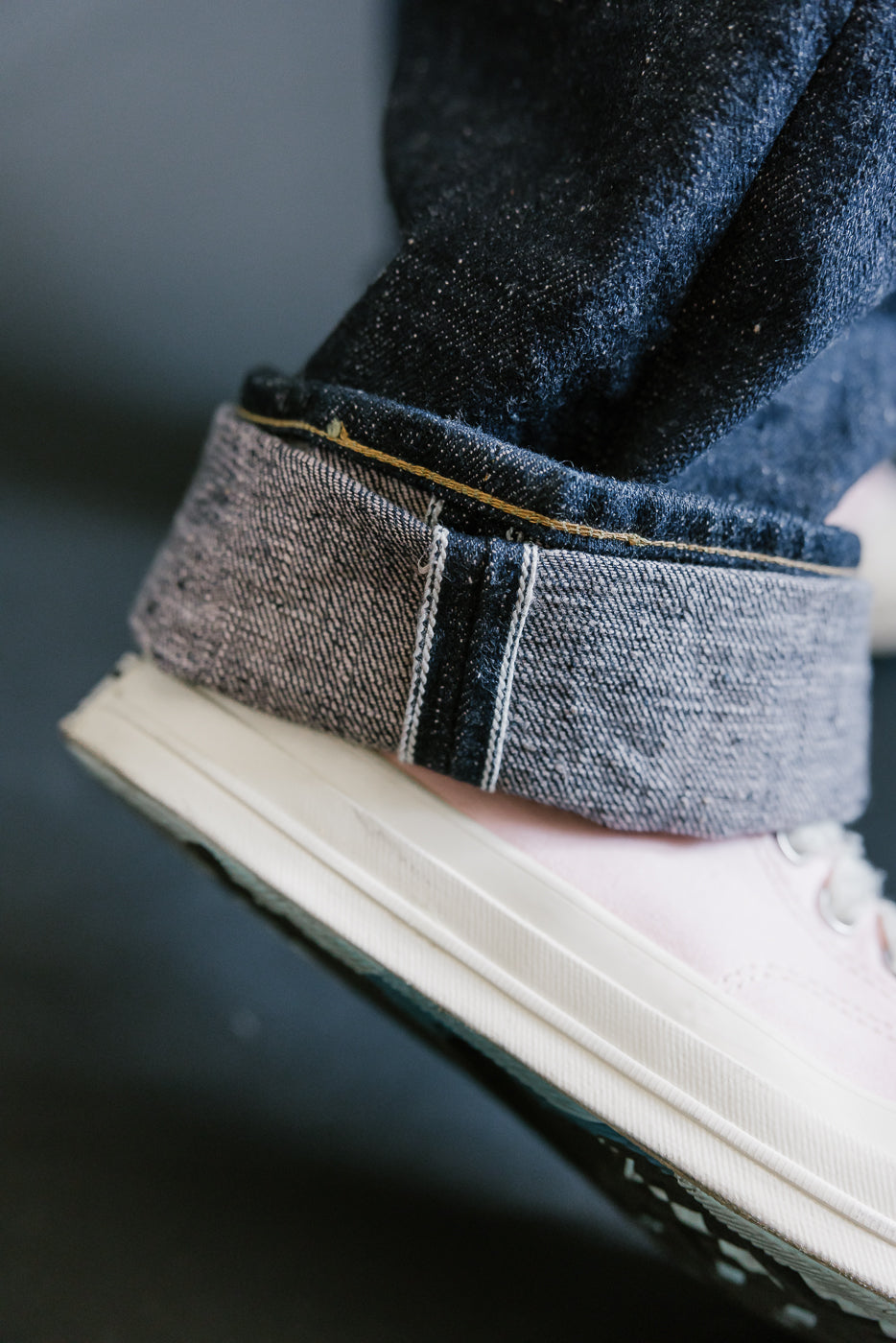 Close-up of Samurai's S500AX-SAKURA jeans, showcasing dark indigo selvedge denim with sakura-dyed weft and a rolled cuff revealing pale grey edge.