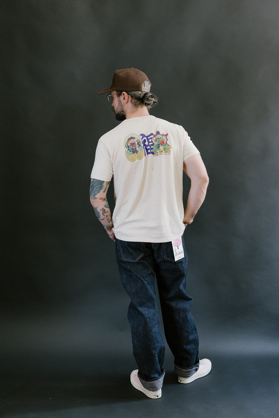 Man wearing Samurai’s S500AX-SAKURA 18oz Ai-Plus-Sakura Selvedge Jeans, showcasing their regular straight fit and distinct paper hangtag on the back pocket.