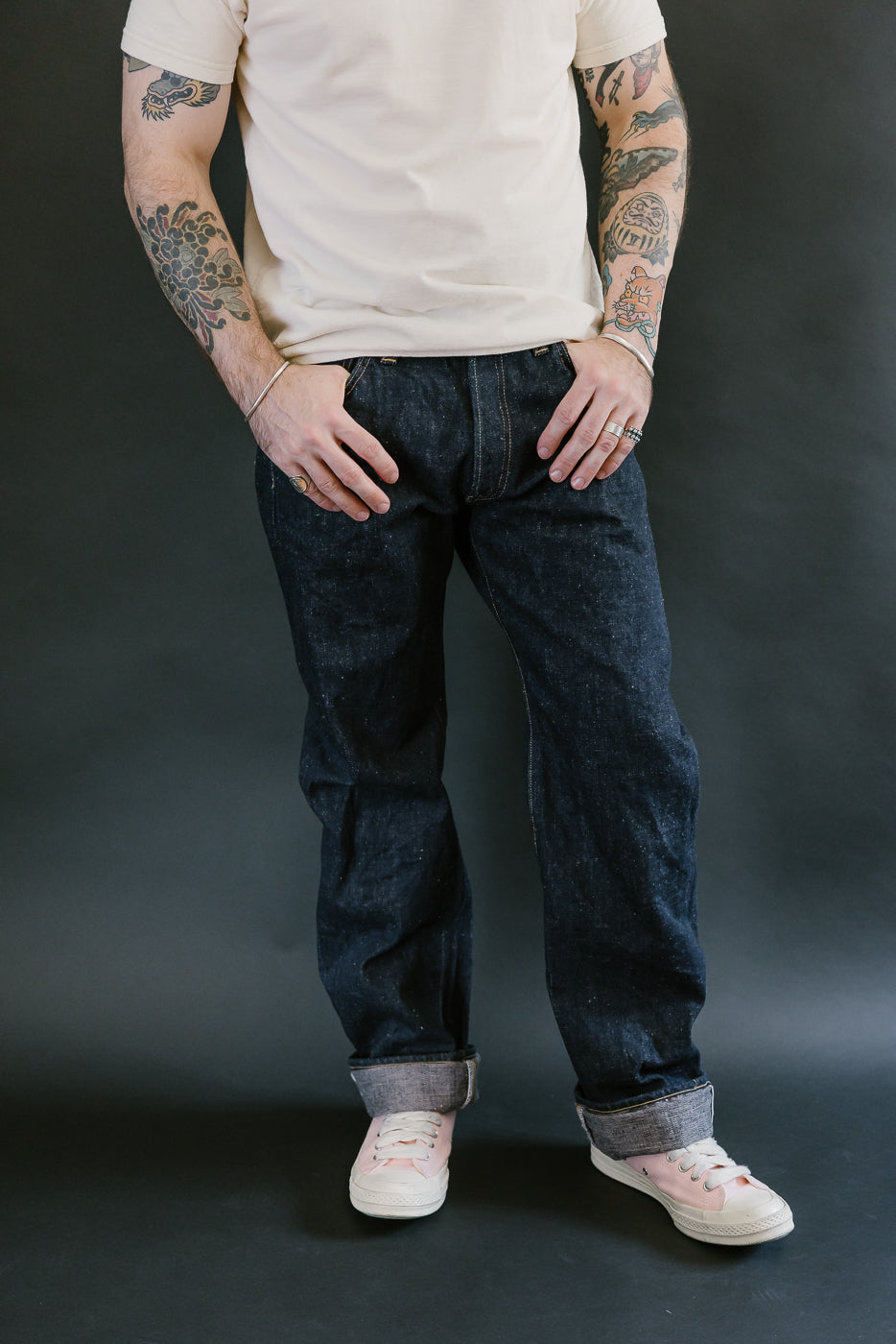 Person wearing S500AX-SAKURA 18oz Ai-Plus-Sakura Selvedge Jeans, showing dark indigo denim with sakura-dyed undertones, rolled cuffs, and pink sneakers.