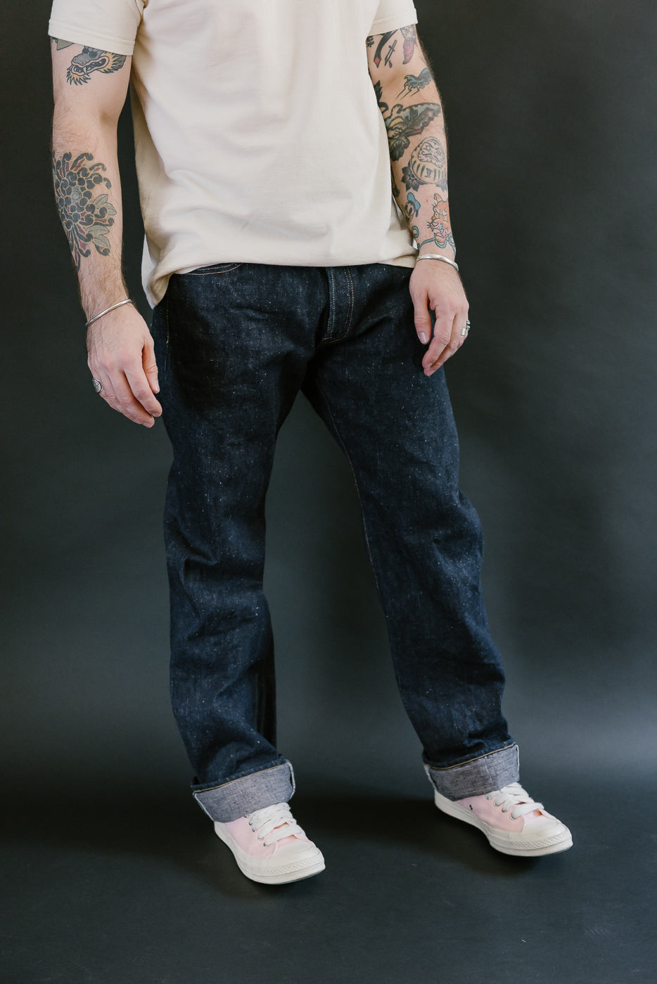 S500AX-SAKURA jeans in dark selvedge denim with sakura-dyed details, worn with a cream tee and pink canvas sneakers, showcasing detailed tattoos and accessories.