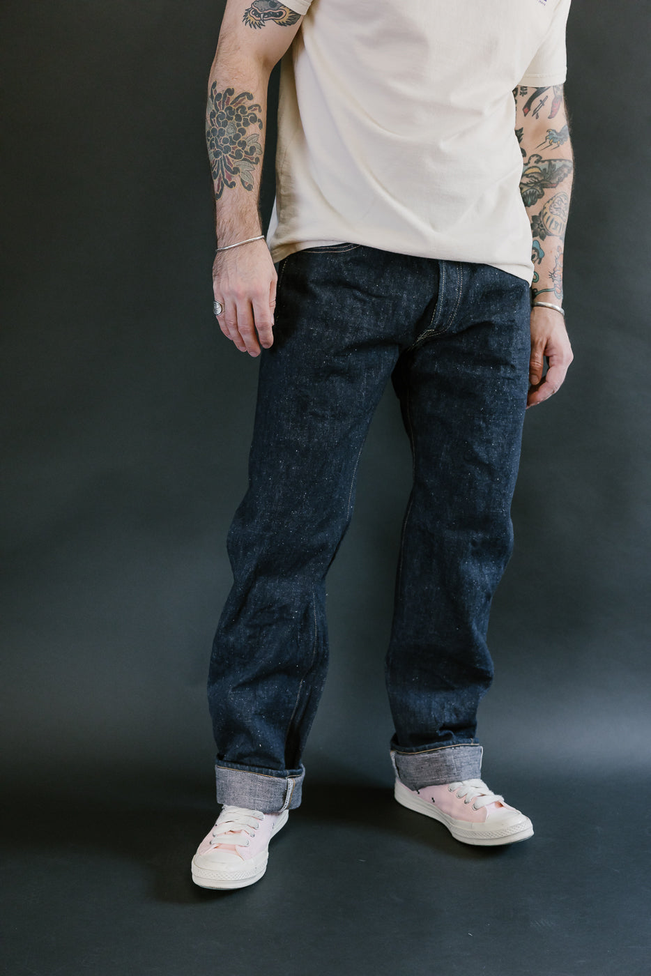 S500AX-SAKURA - 18oz Ai-Plus-Sakura Selvedge Jeans in dark indigo with pink undertones, worn with pale pink sneakers and silver jewelry against a dark backdrop.