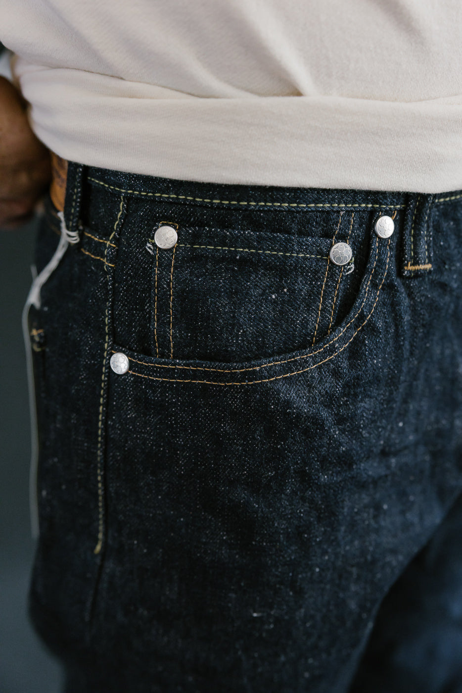 Close-up of Samurai’s S500AX-SAKURA jeans showcasing dark indigo denim with sakura-dyed weft, visible coin pocket, contrast stitching, and tucked-in off-white T-shirt.