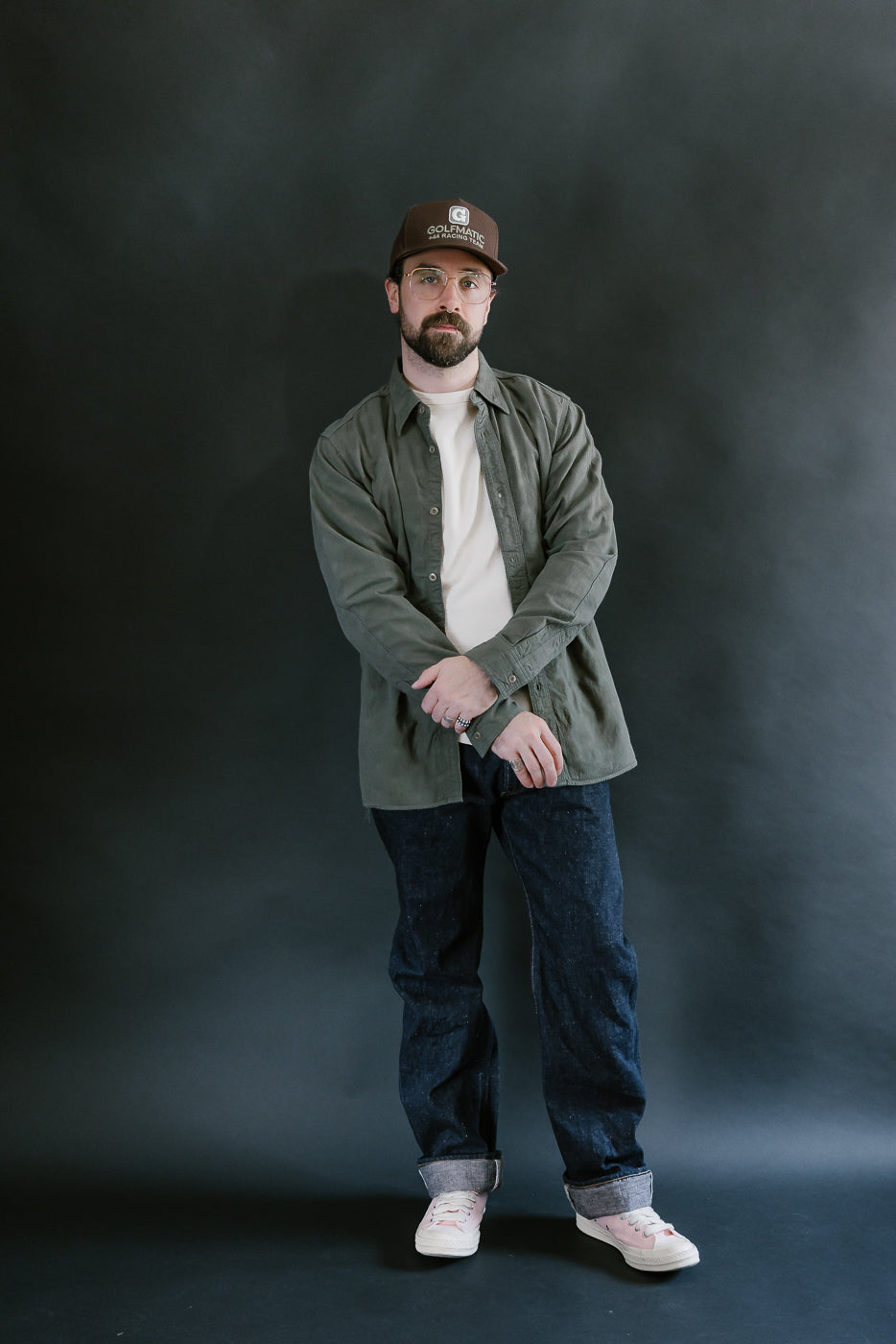 Man wearing the SSS25-ATW Tropical Weather Dobby Shirt in olive green, styled with jeans and sneakers, showcasing a relaxed, contemporary look.