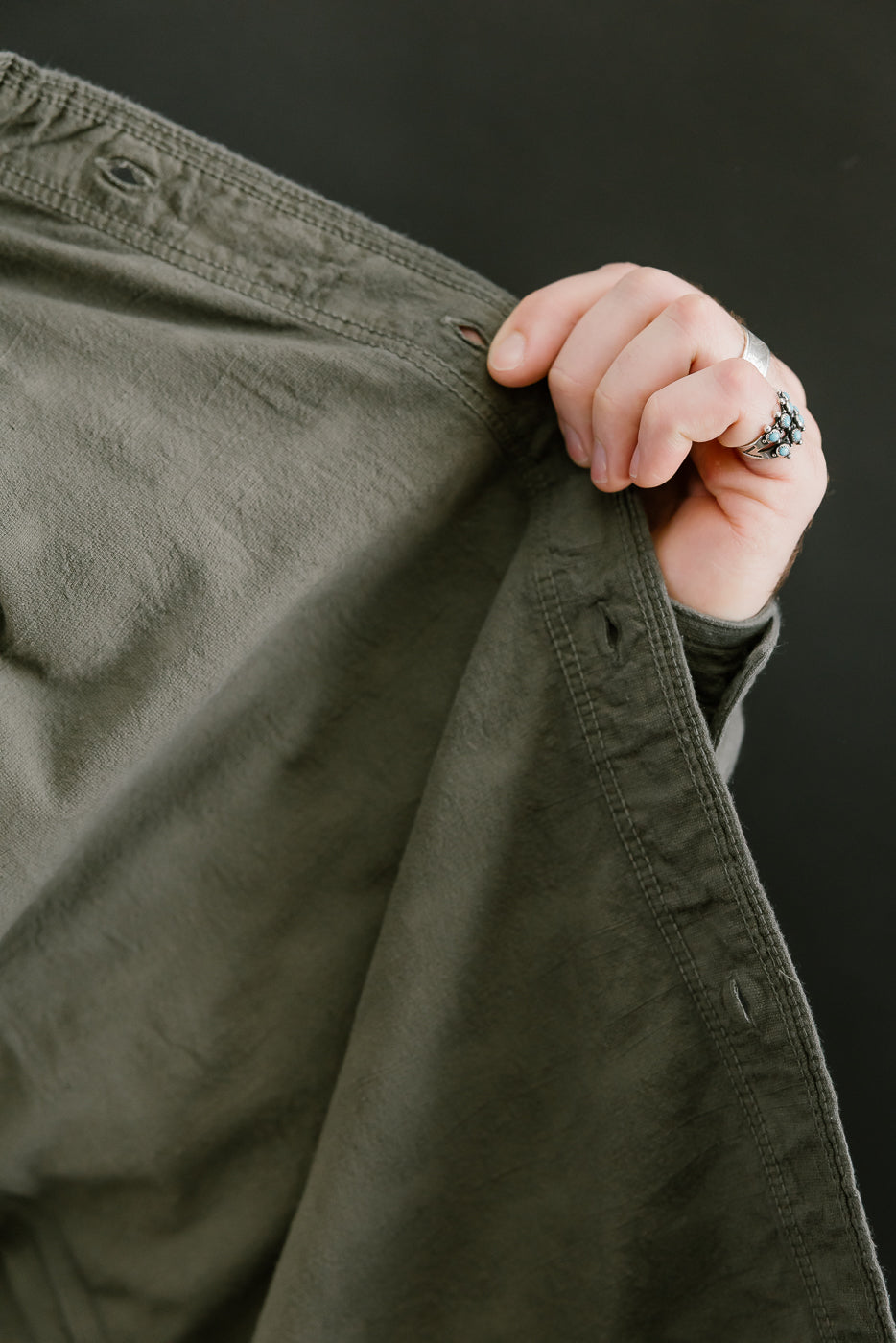 Hand holding olive-green Tropical Weather Dobby Shirt fabric, highlighting its textured 6 oz Japanese Panama-weave, showcasing craftsmanship and style from Dant's premium menswear collection.