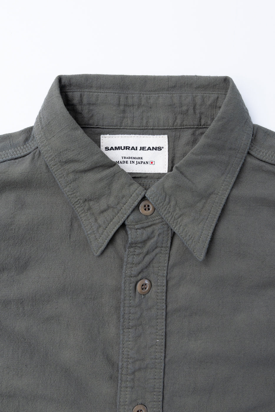 Close-up of SSS25-ATW Tropical Weather Dobby Shirt in muted gray-olive, showcasing the collar, placket, and Samurai Jeans label with Japanese flag icon.