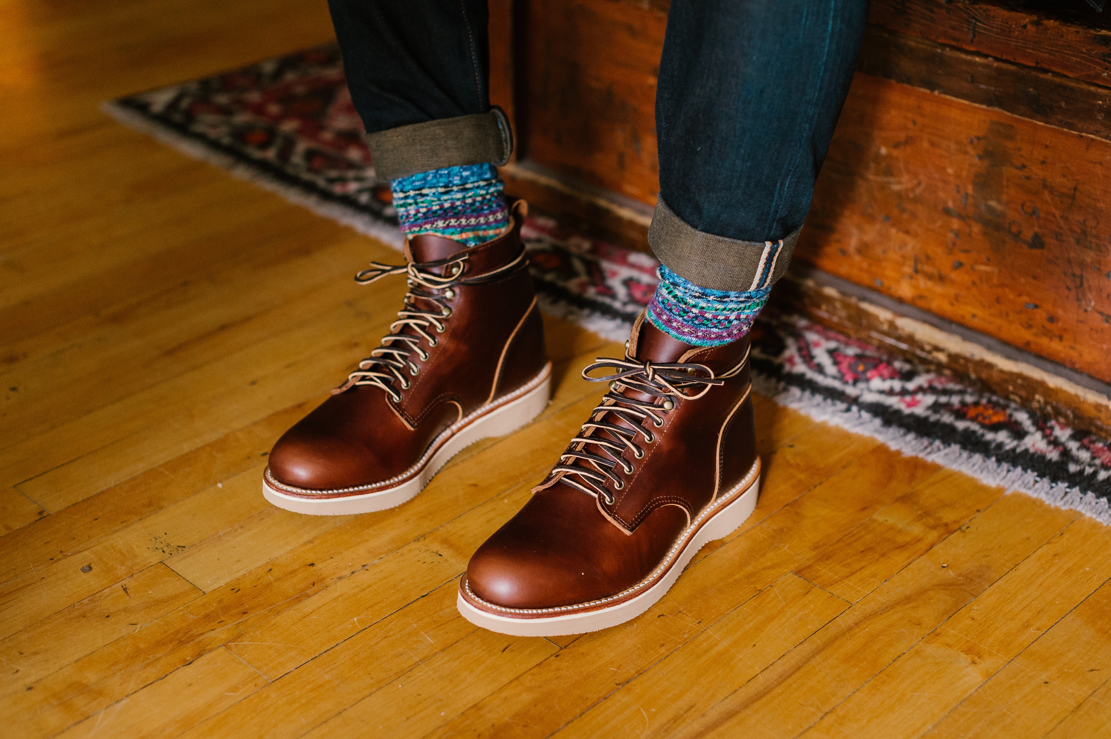 Brown leather boots, colorful socks, and cuffed selvedge denim on wood floor at Dant store