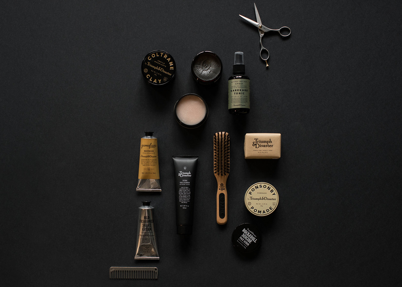 Men’s grooming products, wooden brush, scissors, and comb arranged on a dark background.