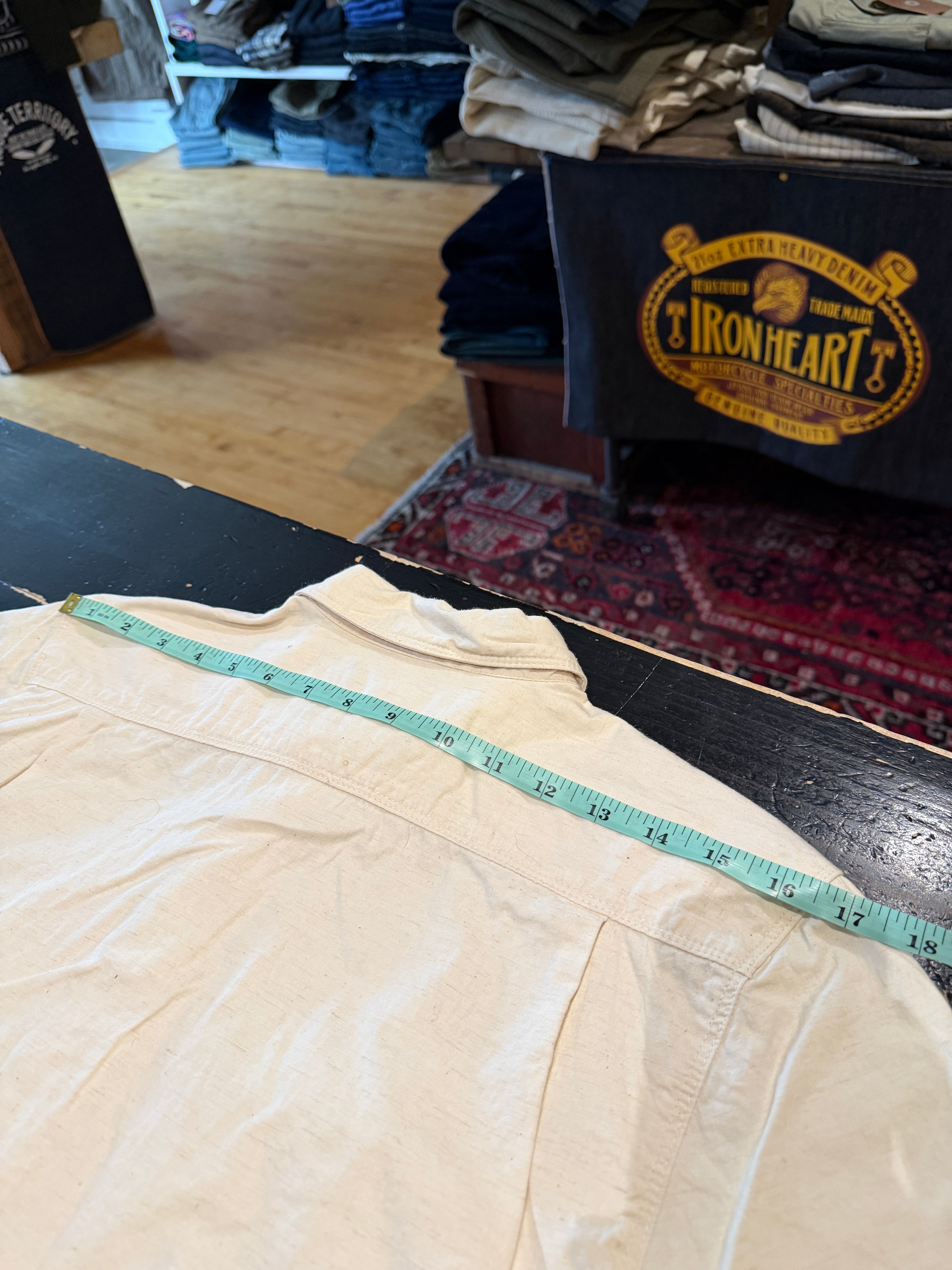 Close-up of the back yoke of an off-white shirt flat lay, measuring shoulder width with tape.