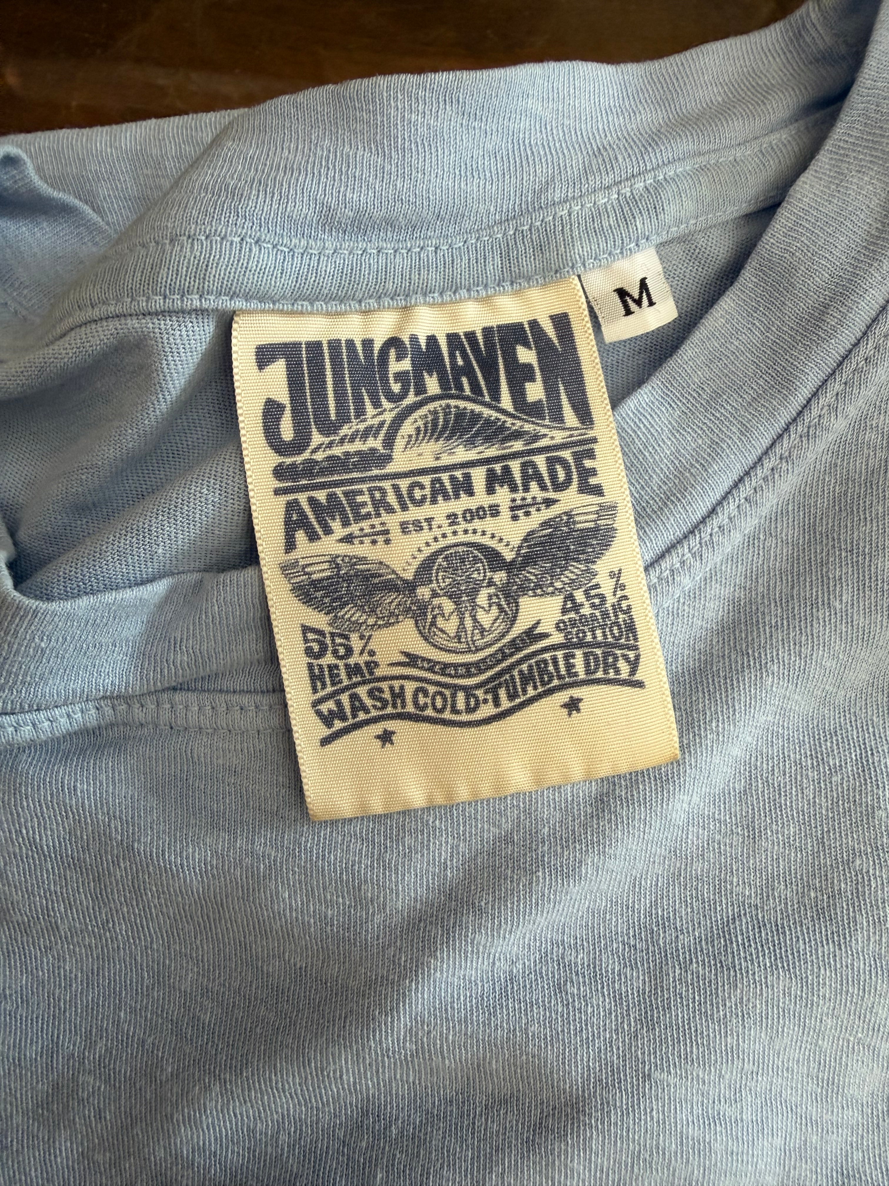 Close-up of Jungmaven shirt tag showing 55% hemp, 45% organic cotton, American made details on light gray fabric.