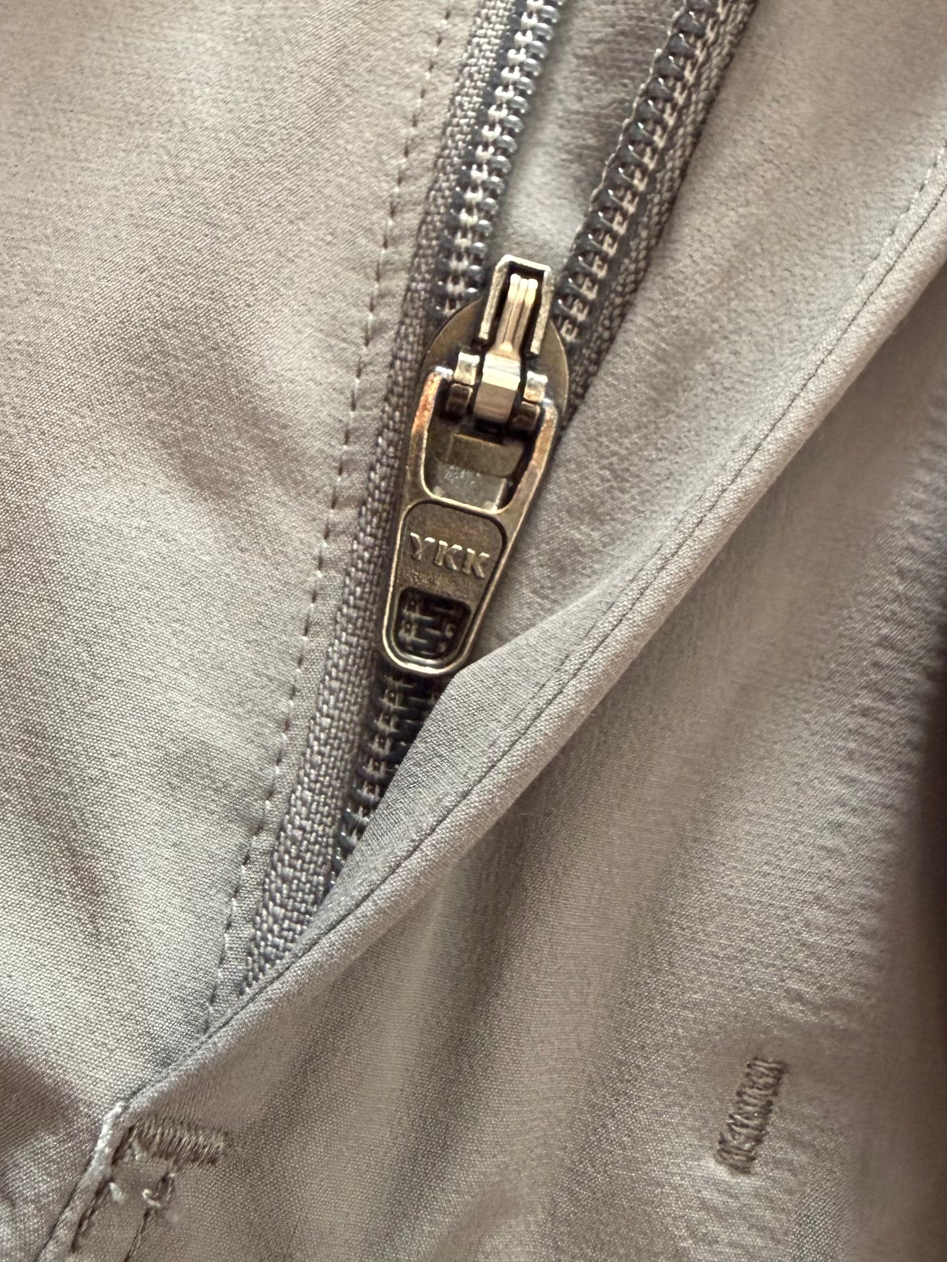 Close-up of YKK zipper on gray garment, showcasing fabric texture and stitching detail
