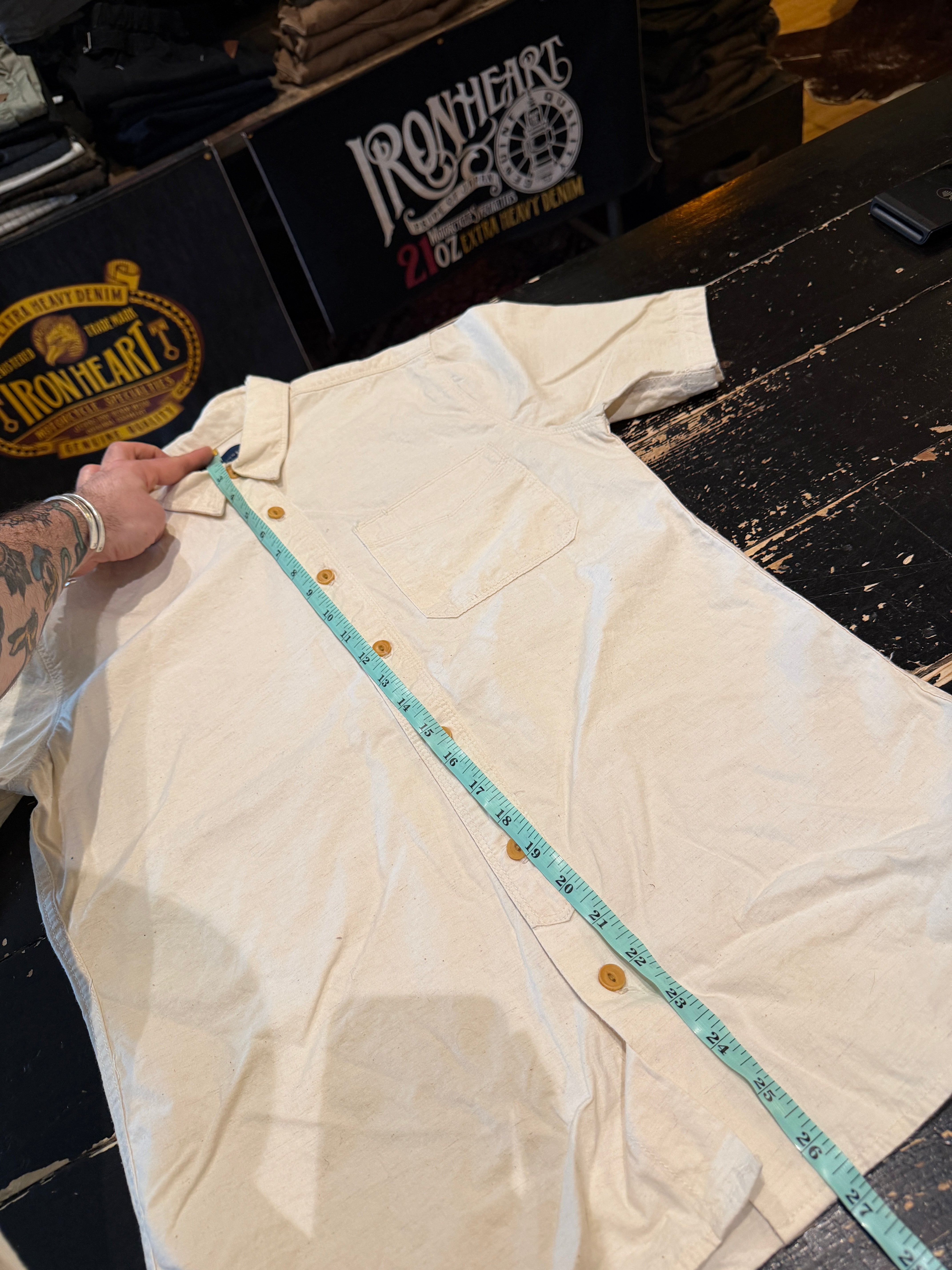 Flat lay front view of short-sleeve cream button-up shirt measured with tape, pocket visible.