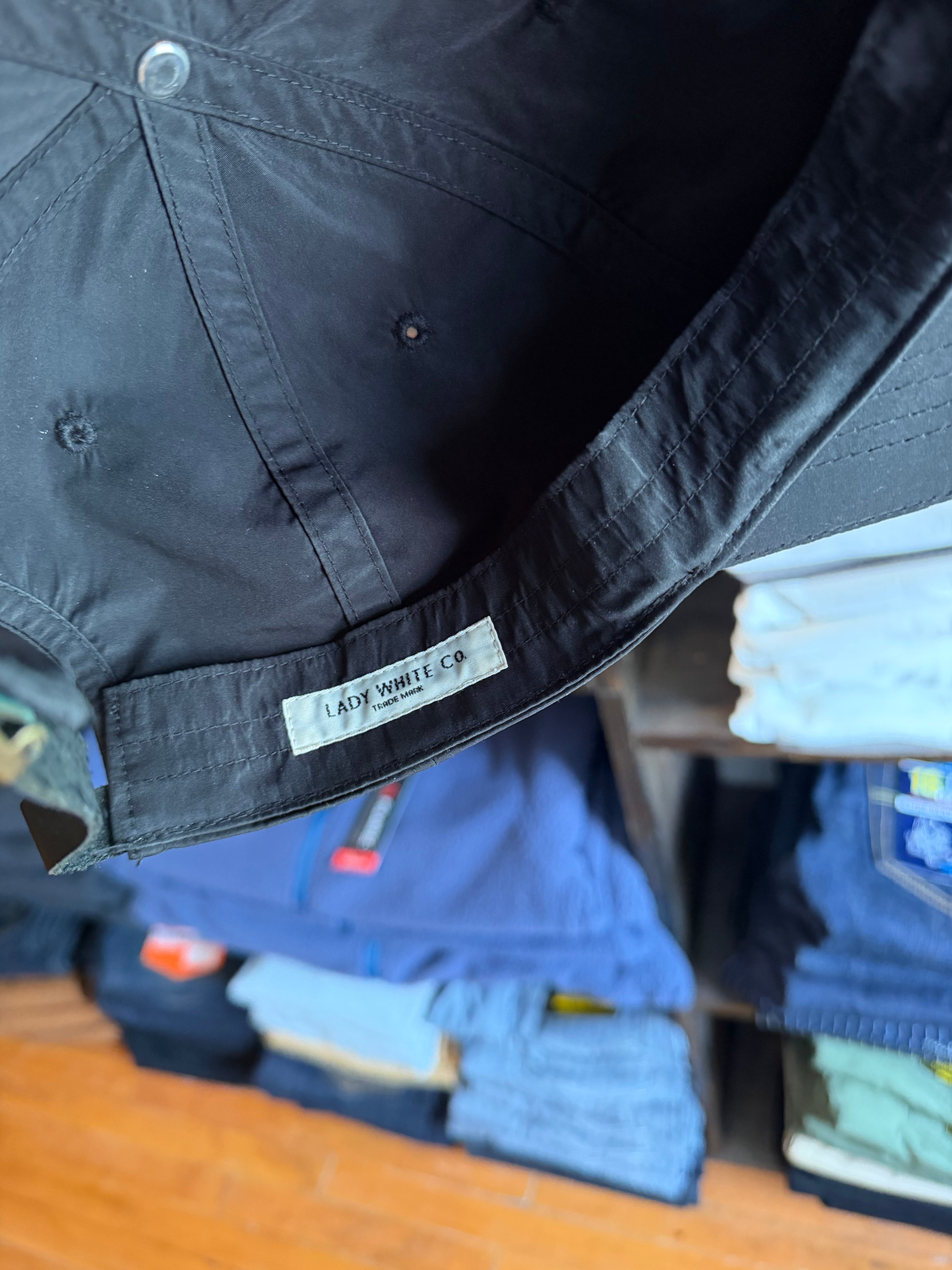 Close-up of black cap's interior showing Lady White Co. tag, button details, and fabric texture.