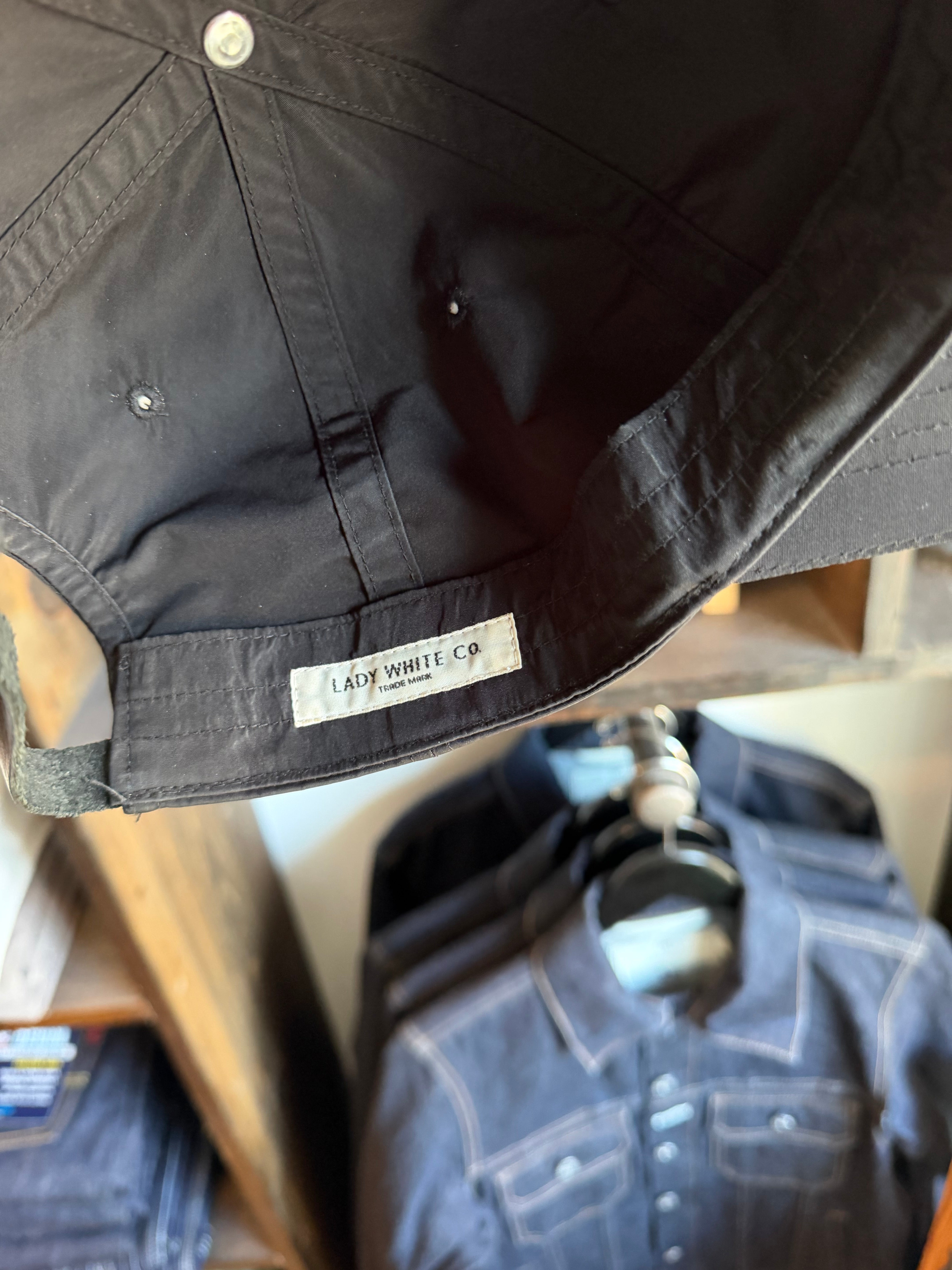 Close-up of black cap's interior showing Lady White Co. tag, fabric texture, and stitching details.