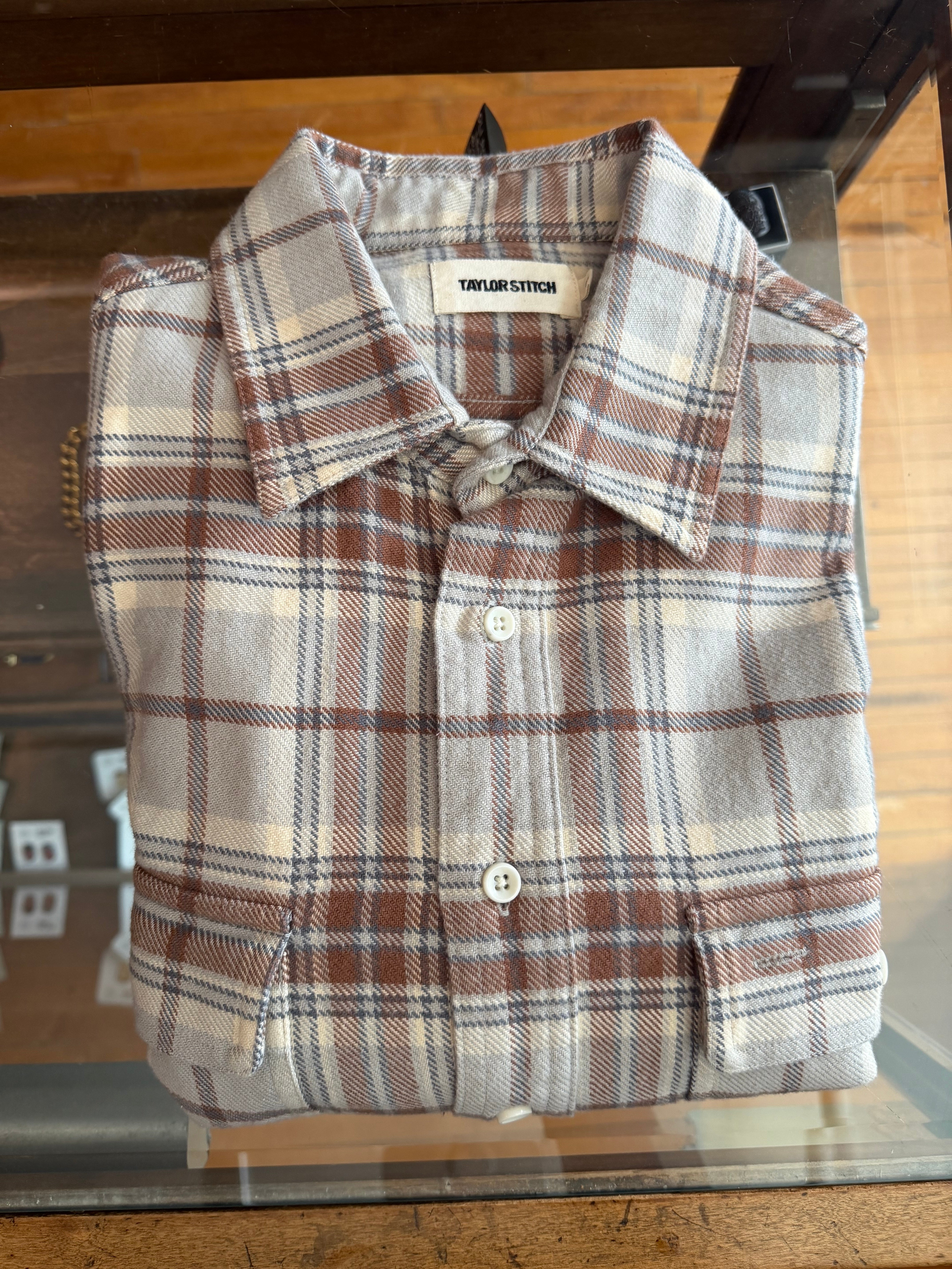 Front flat lay of folded Taylor Stitch plaid flannel shirt with white buttons and spread collar, displayed at Dant apparel store.