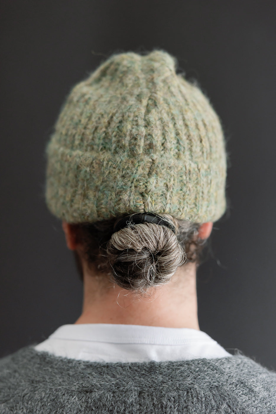 Close-up back view of a textured sage green knit beanie on a male model.