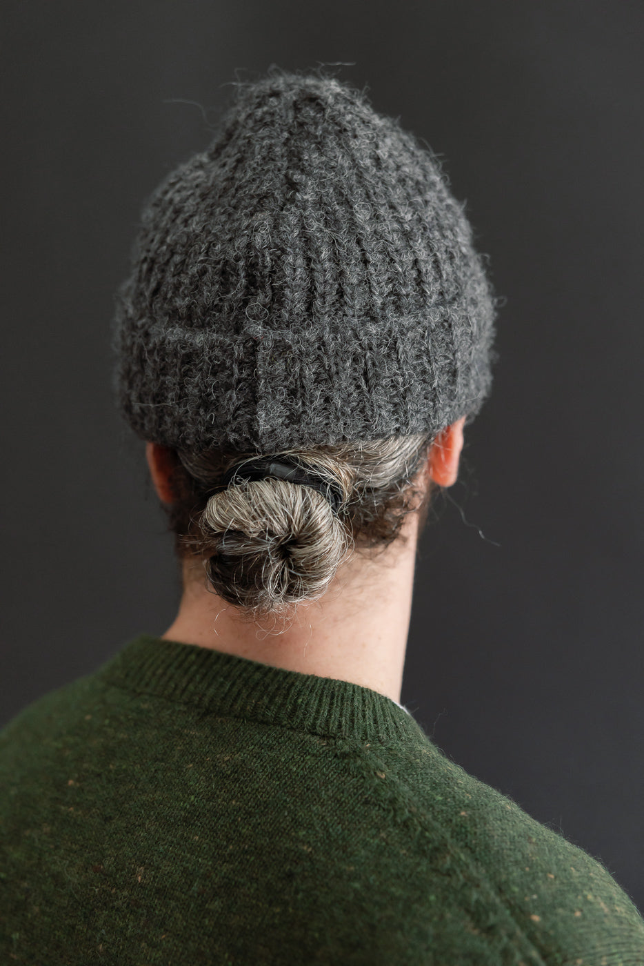 Close-up back view of a male model wearing a grey textured knit beanie and green sweater.