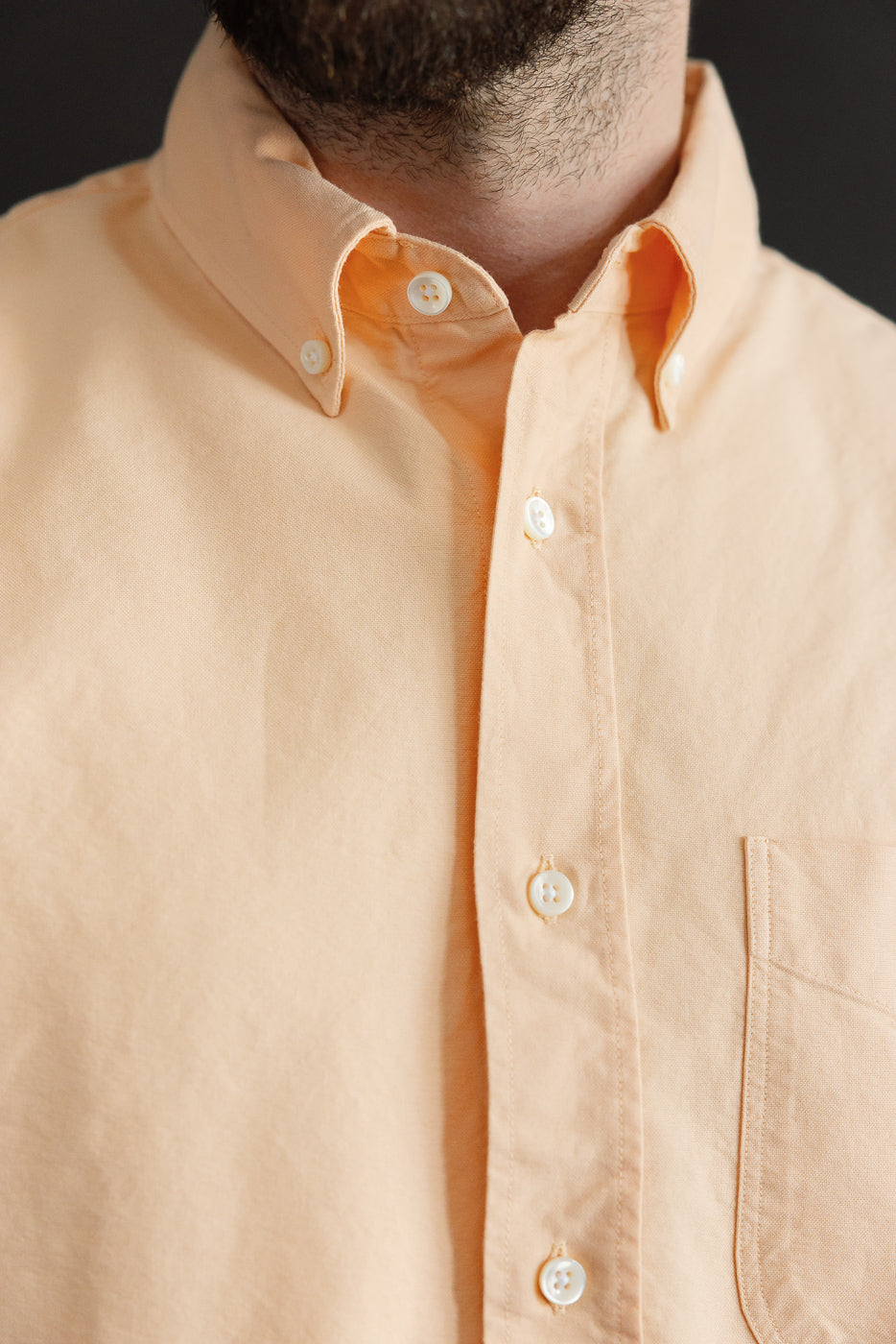 Close-up front view of peach button-down shirt, male model, athletic build, showing collar and buttons