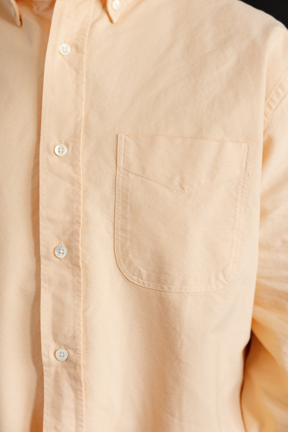 Close-up front view of peach button-down shirt with chest pocket, white buttons, and textured fabric on male model.