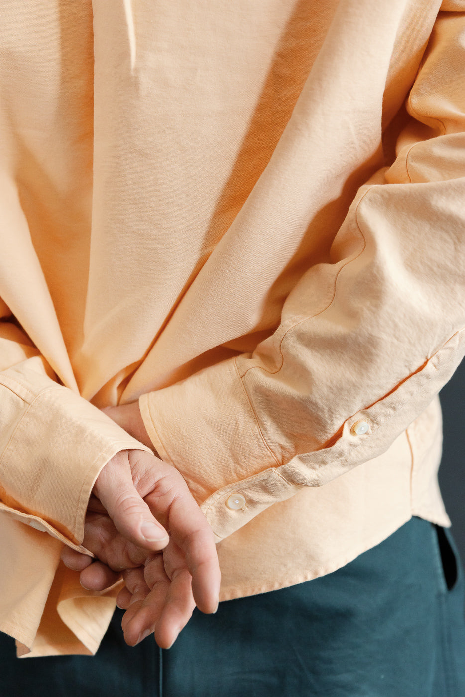 Close-up front view of peach long-sleeve shirt on male model, showing button cuffs and fabric texture