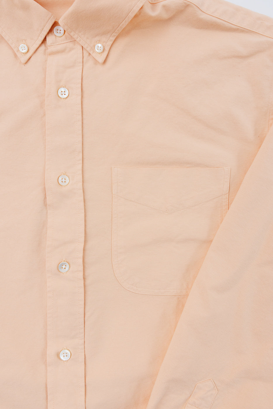 Close-up front view of peach button-down shirt with button collar, chest pocket, and white buttons