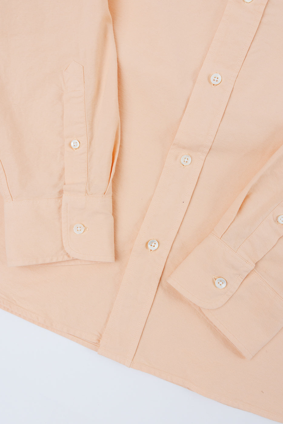 Close-up front view of peach button-down shirt, showcasing fabric texture, white buttons, and sleeve details.