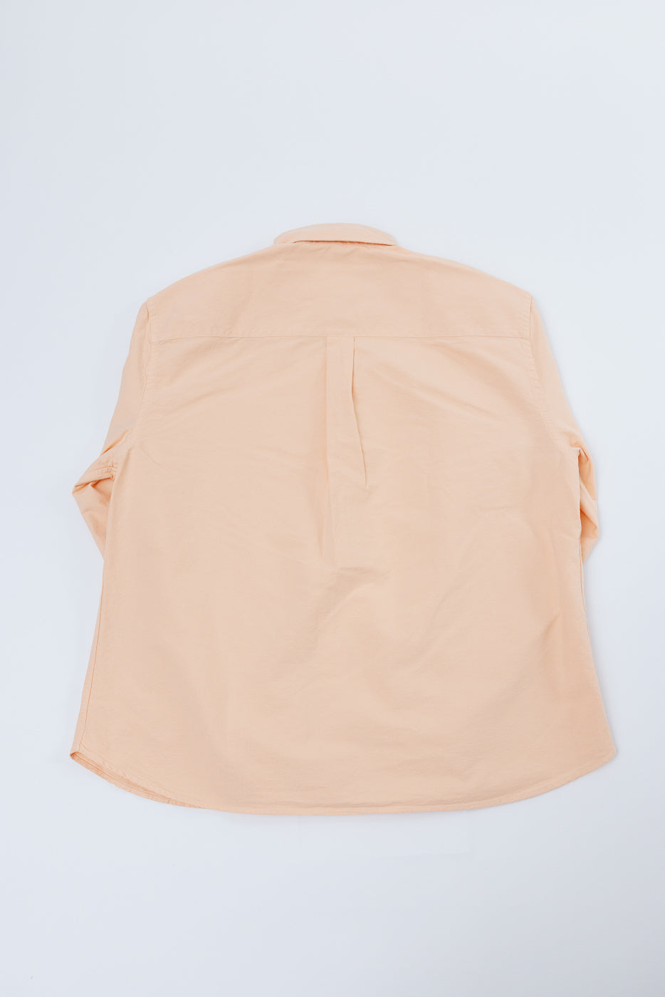Back view of peach long-sleeve shirt, flat lay, showing collar, yoke, and curved hem