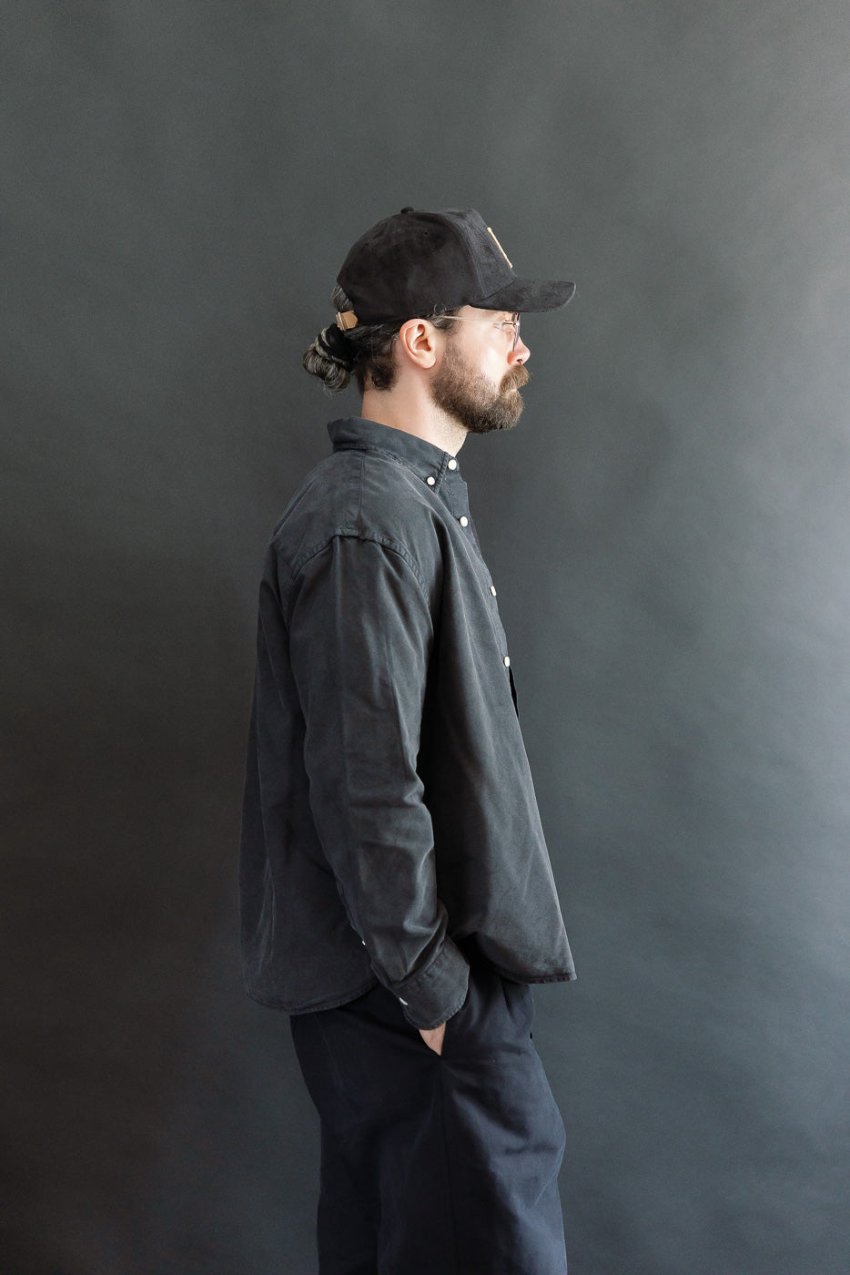 Side view full-body of male model 5'9, 165lbs athletic build wearing vintage black oxford cotton shirt from Dant, showing shirt's profile and relaxed fit.