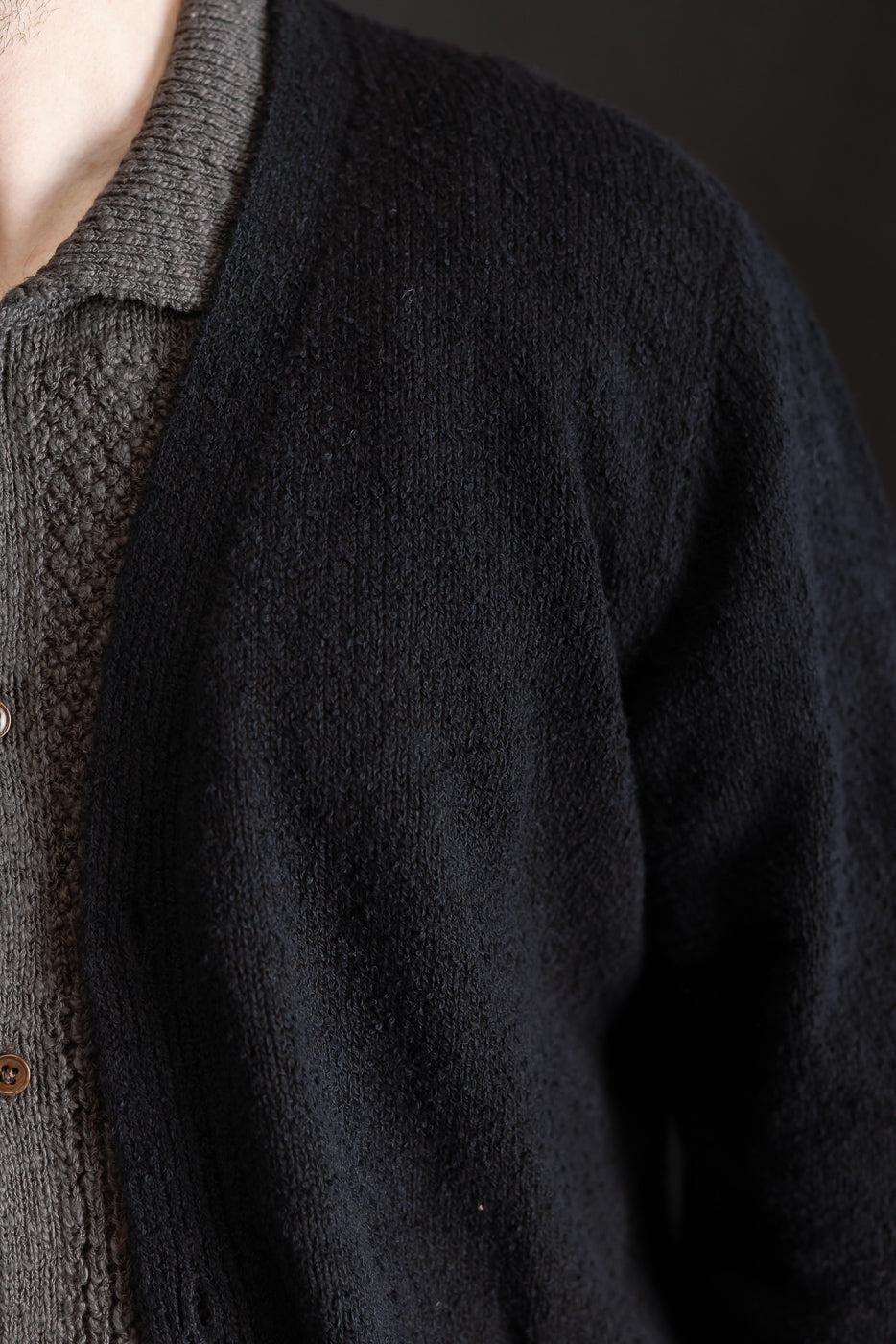 Close-up of the front left chest of a black boucle cardigan on a male model, showing button and textured knit details.