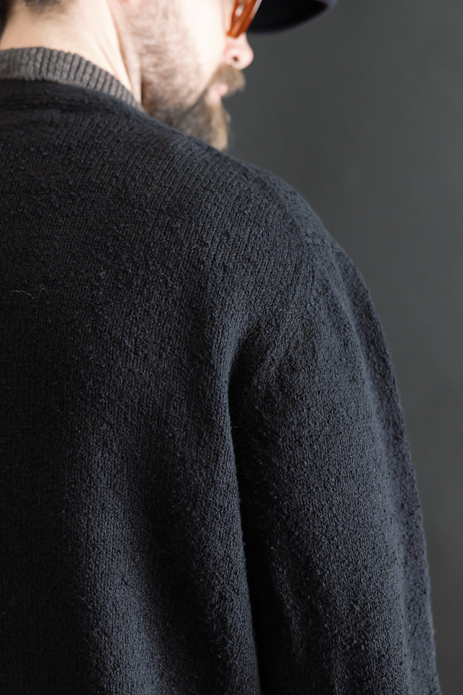 Close-up of back shoulder and upper sleeve detail on black boucle cardigan, worn by male model, 5'9