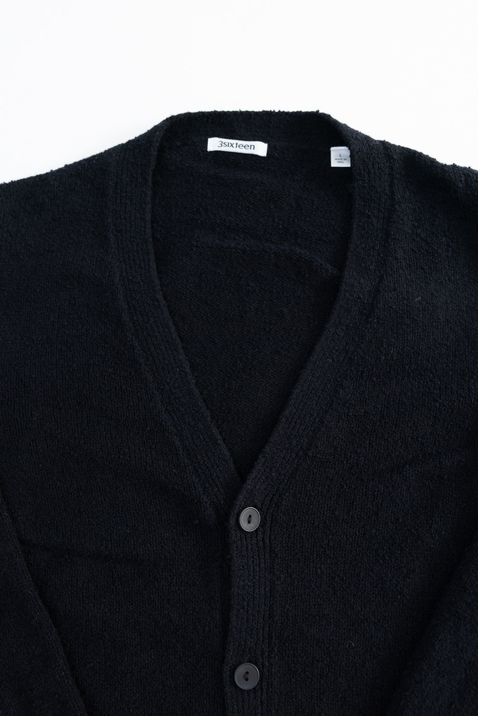 Close-up of black boucle classic cardigan front, showing buttons, v-neck collar, and fabric texture.