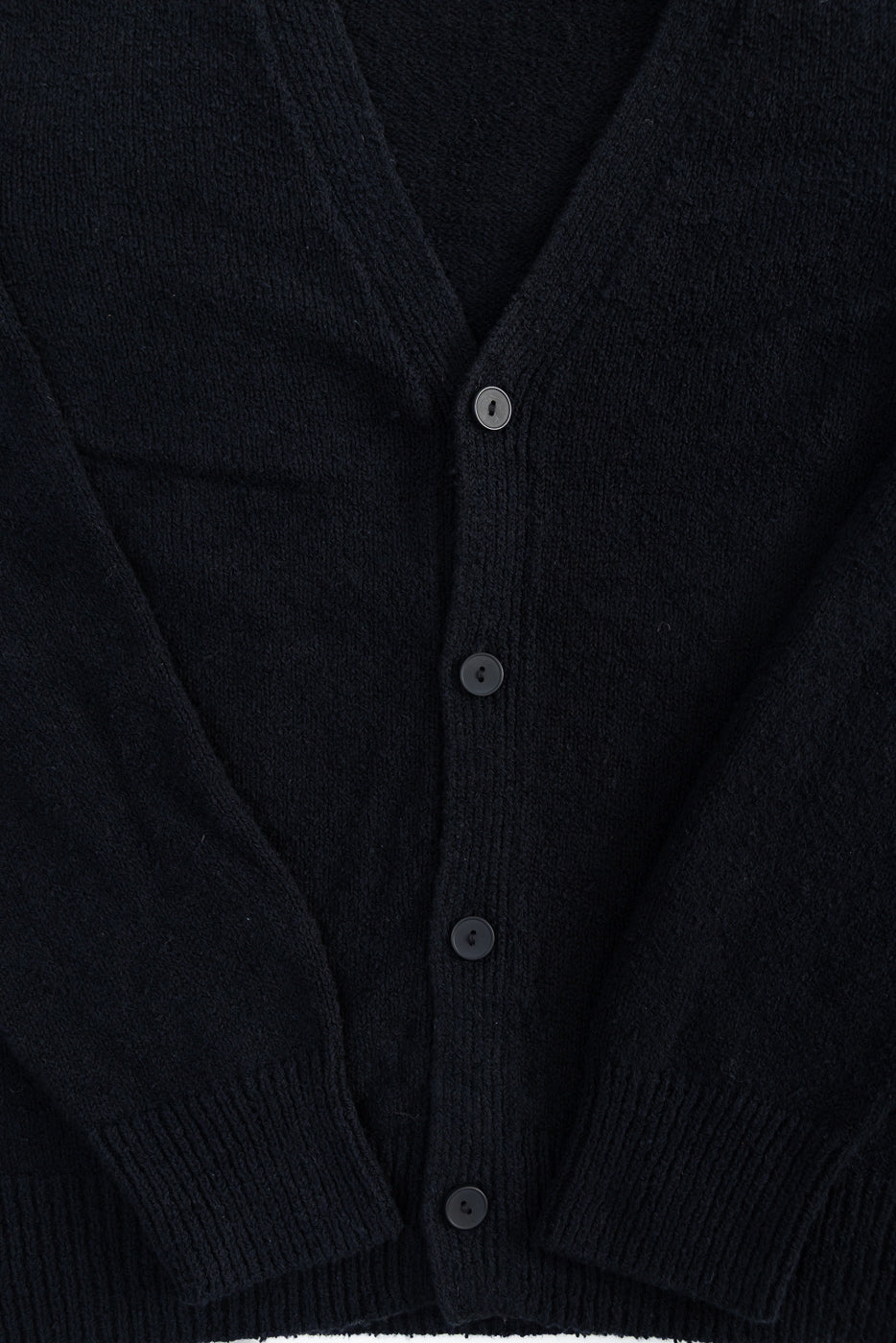 Close-up of front black boucle cardigan fabric texture, center buttons, ribbed cuffs and hem.