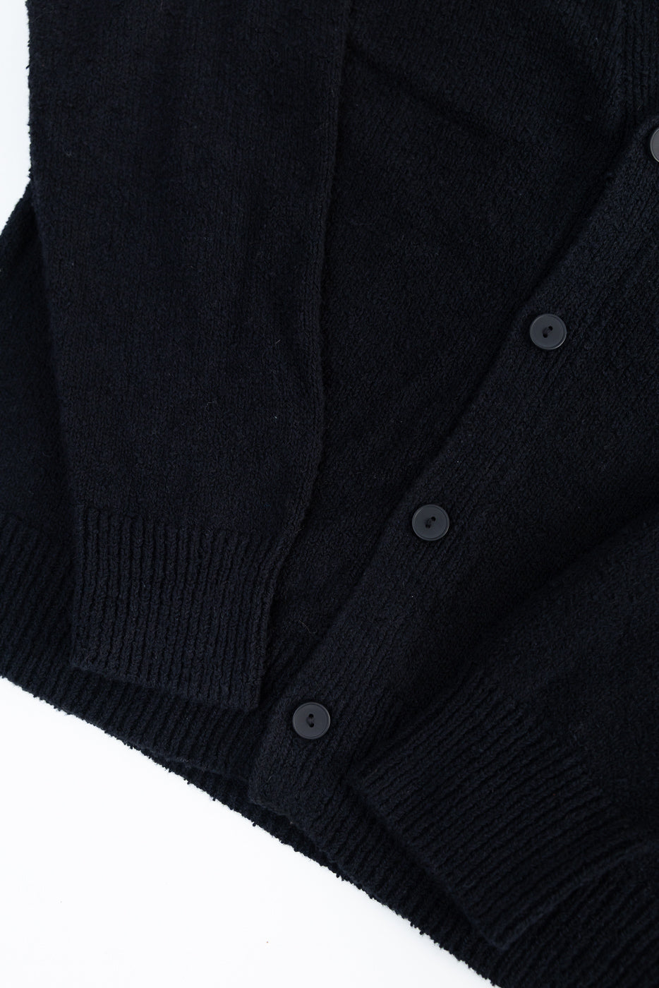 Close-up of black boucle cardigan front, showing buttons, textured knit, ribbed cuff and hem.