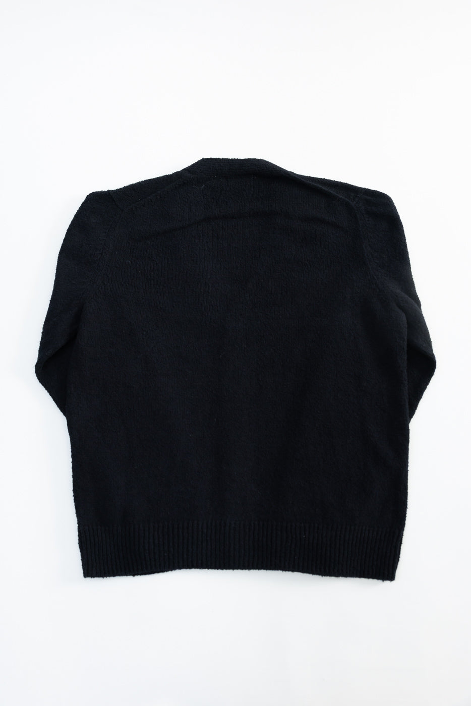 Flat lay of black boucle classic cardigan, back view, showing ribbed hem and fabric texture