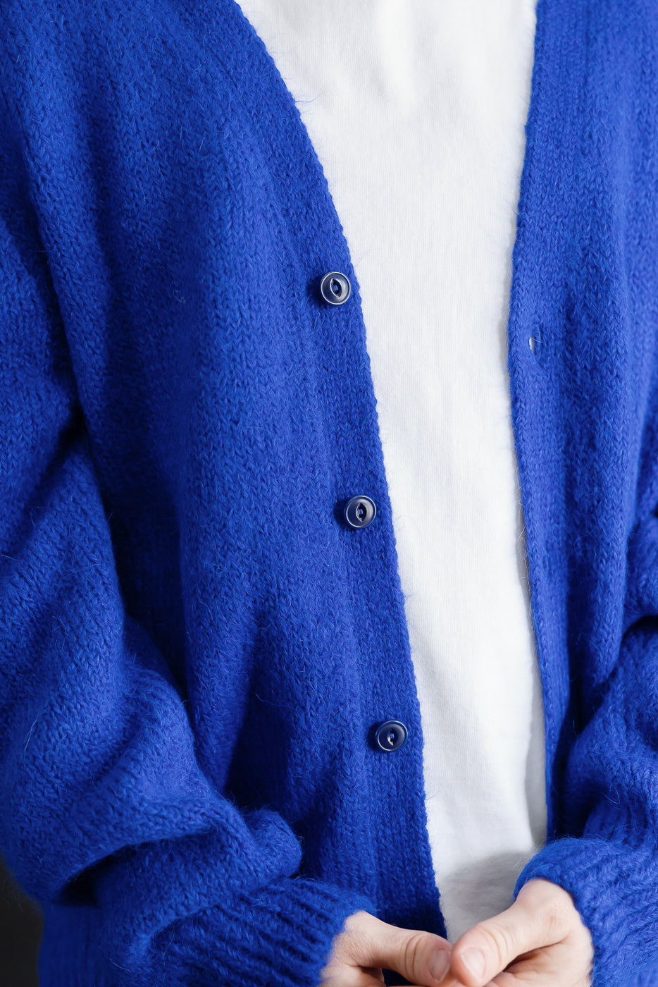 Close-up front view of a blue mohair cardigan with dark buttons over a white t-shirt.