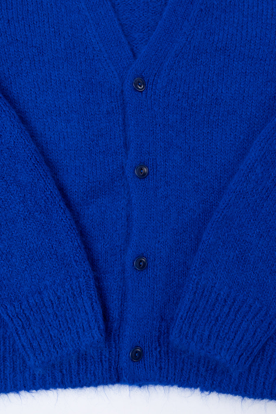 Close-up front view of a royal blue knit cardigan showing button details and fuzzy texture.