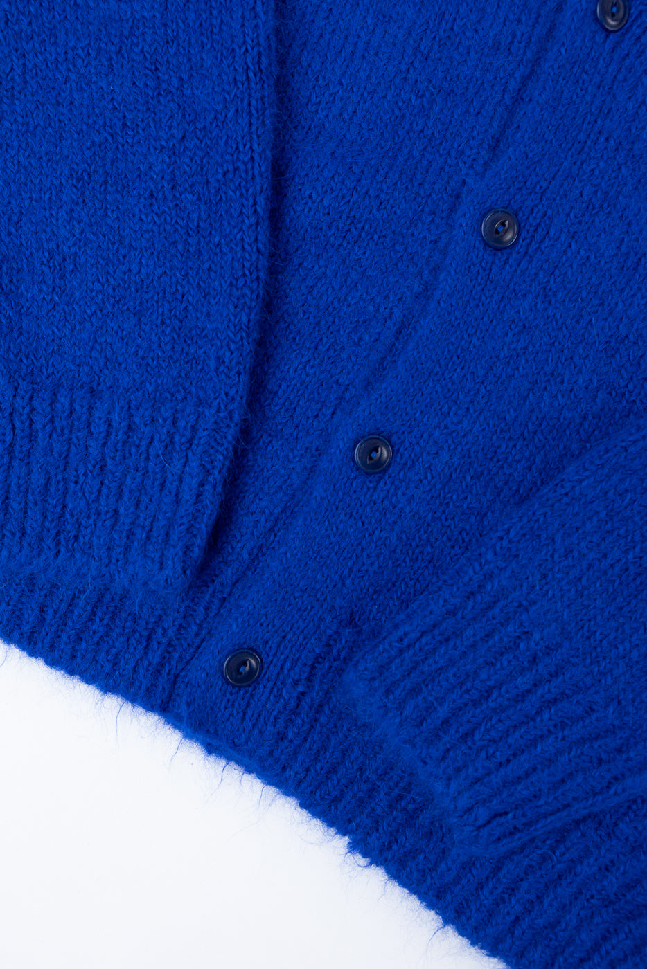 Close-up of the front of a royal blue knit cardigan featuring dark buttons and fuzzy texture.